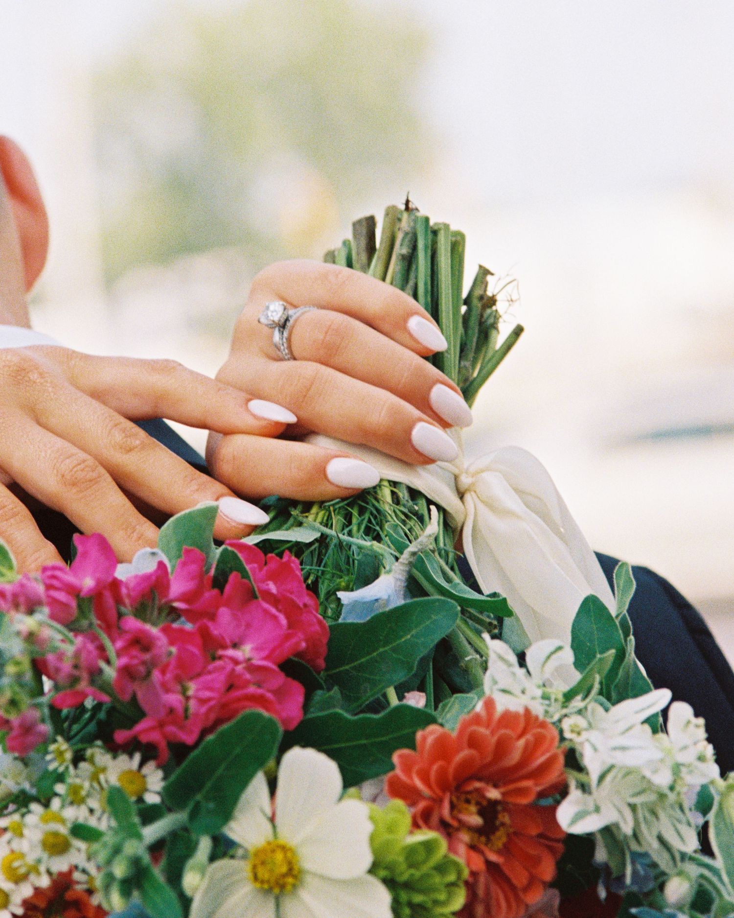 Bride with white manicured nails holding a colorful bridal bouquet with zinnias and greenery.