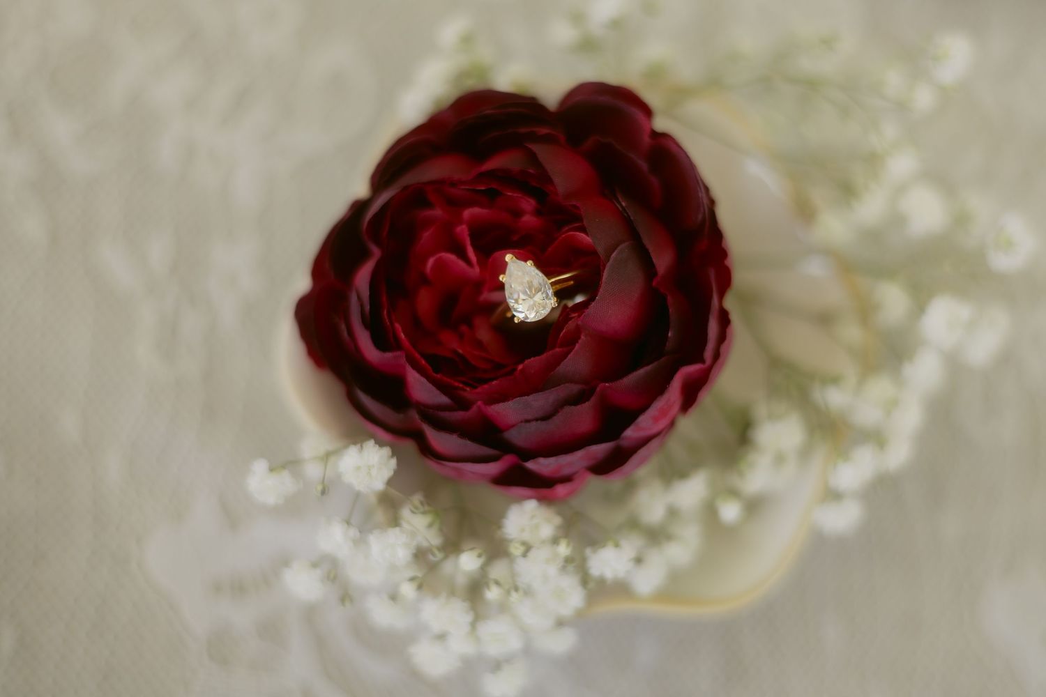 Diamond engagement ring nestled inside a deep red rose surrounded by baby's breath flowers.