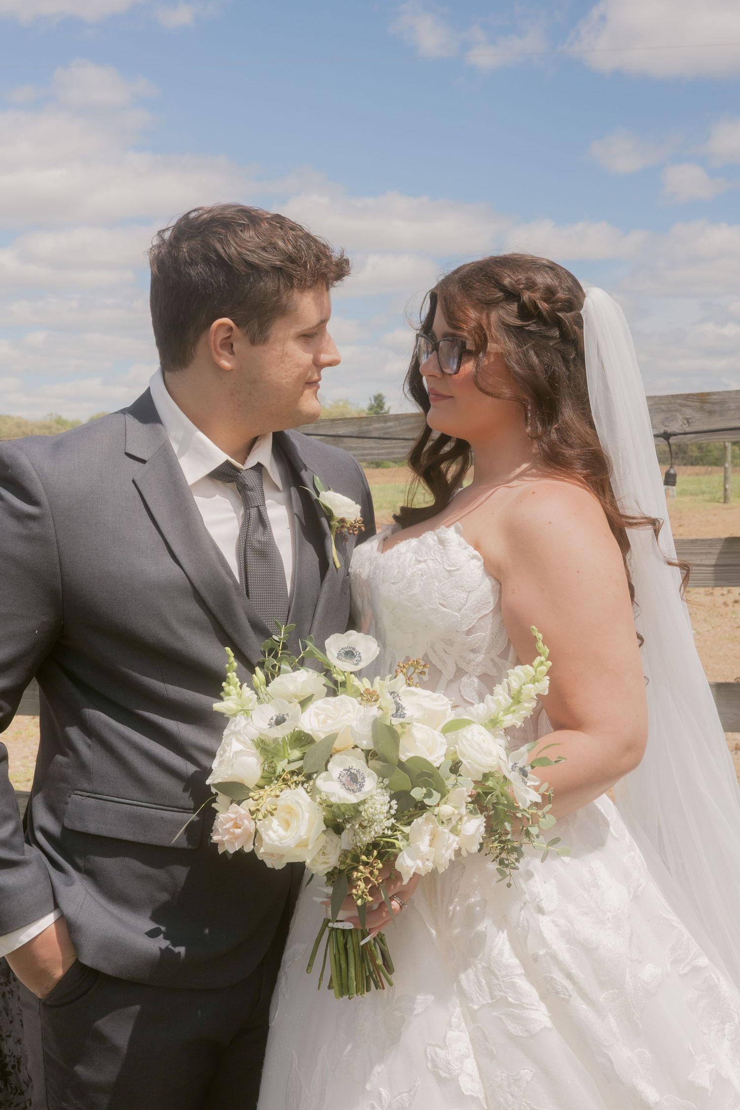 Smiling bride holding white bouquet and groom in gray suit share a joyful outdoor moment.