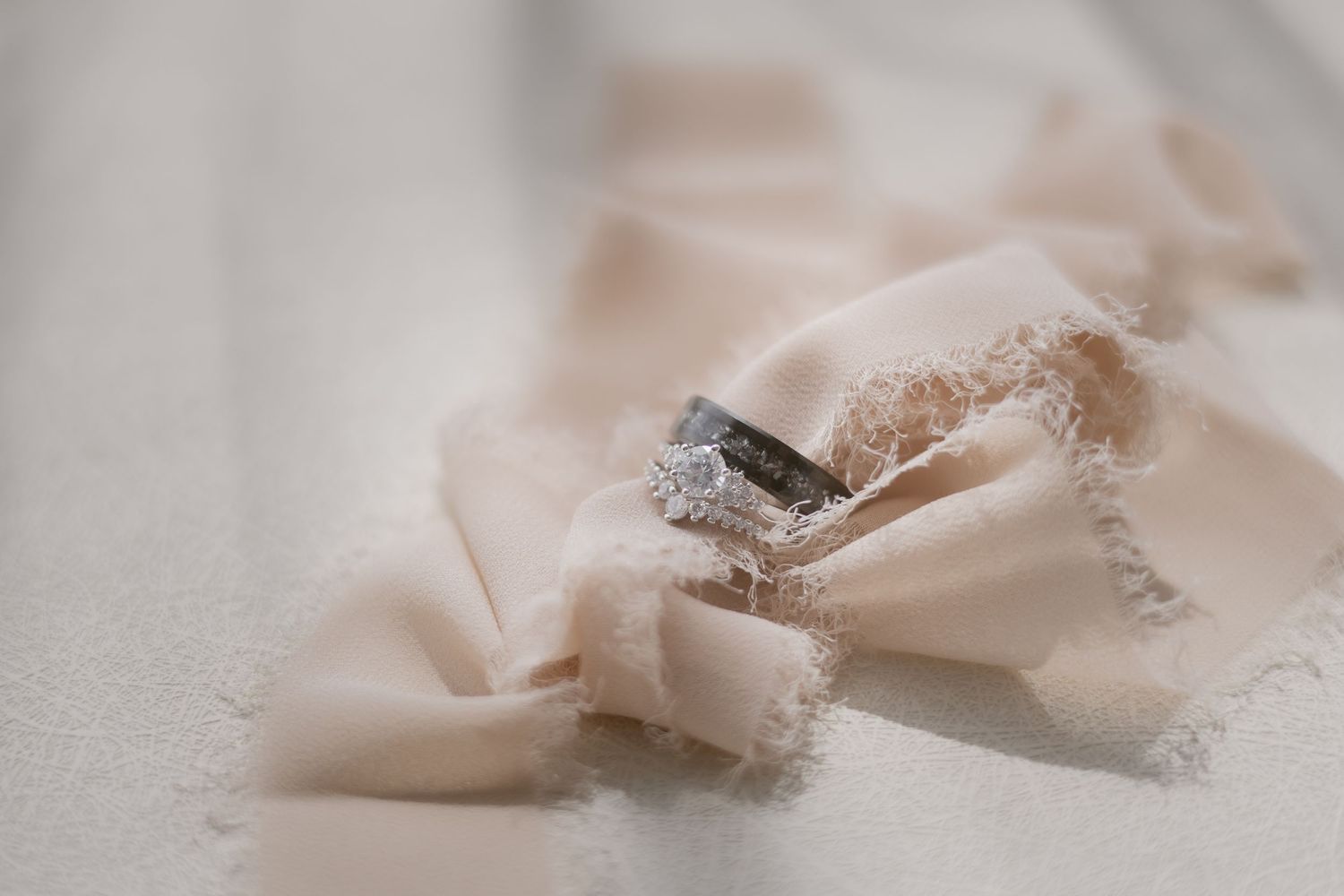 Diamond engagement ring and wedding bands resting on soft cream fabric close-up detail shot.