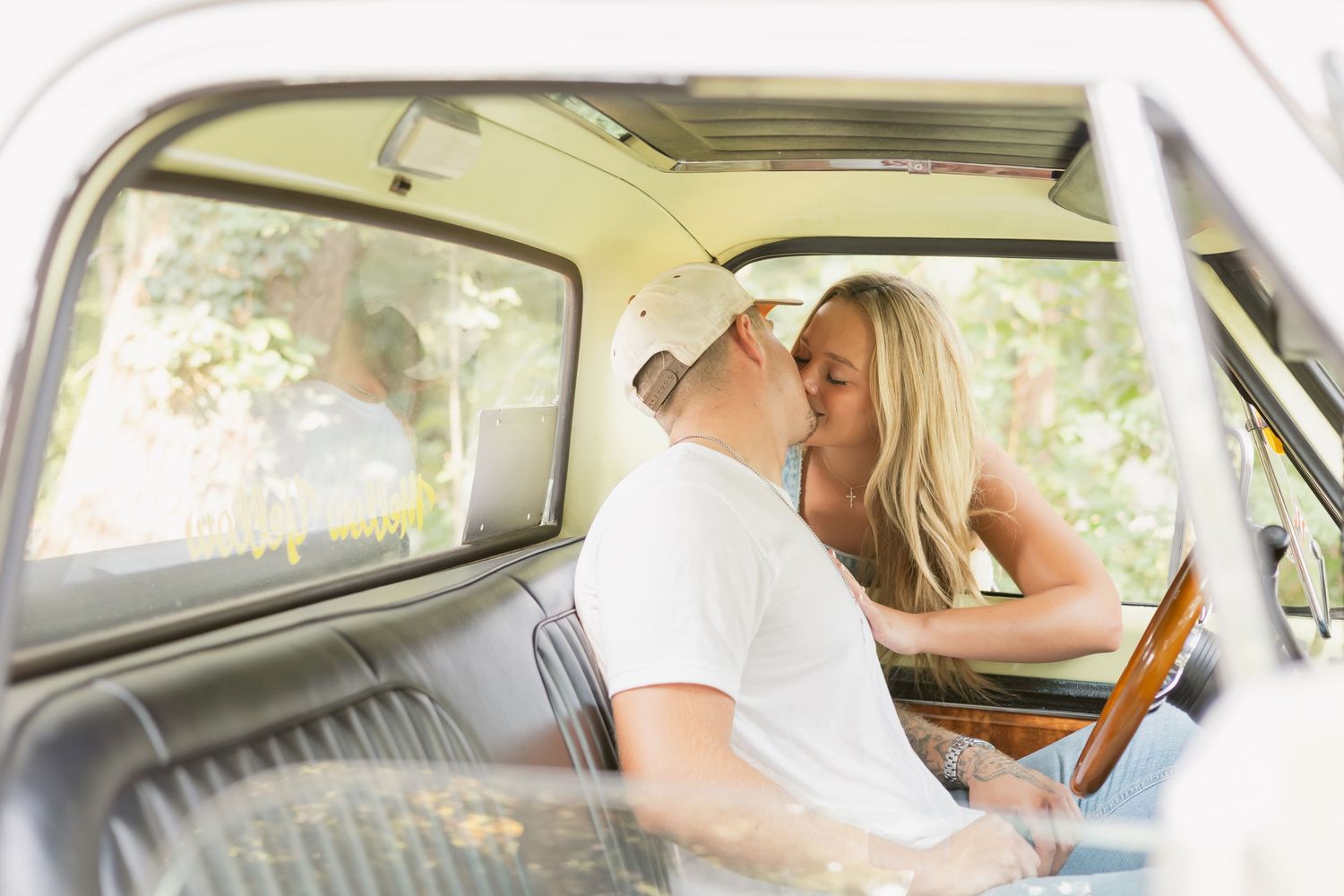 Couple sharing a tender kiss inside a classic vintage vehicle during outdoor engagement shoot.