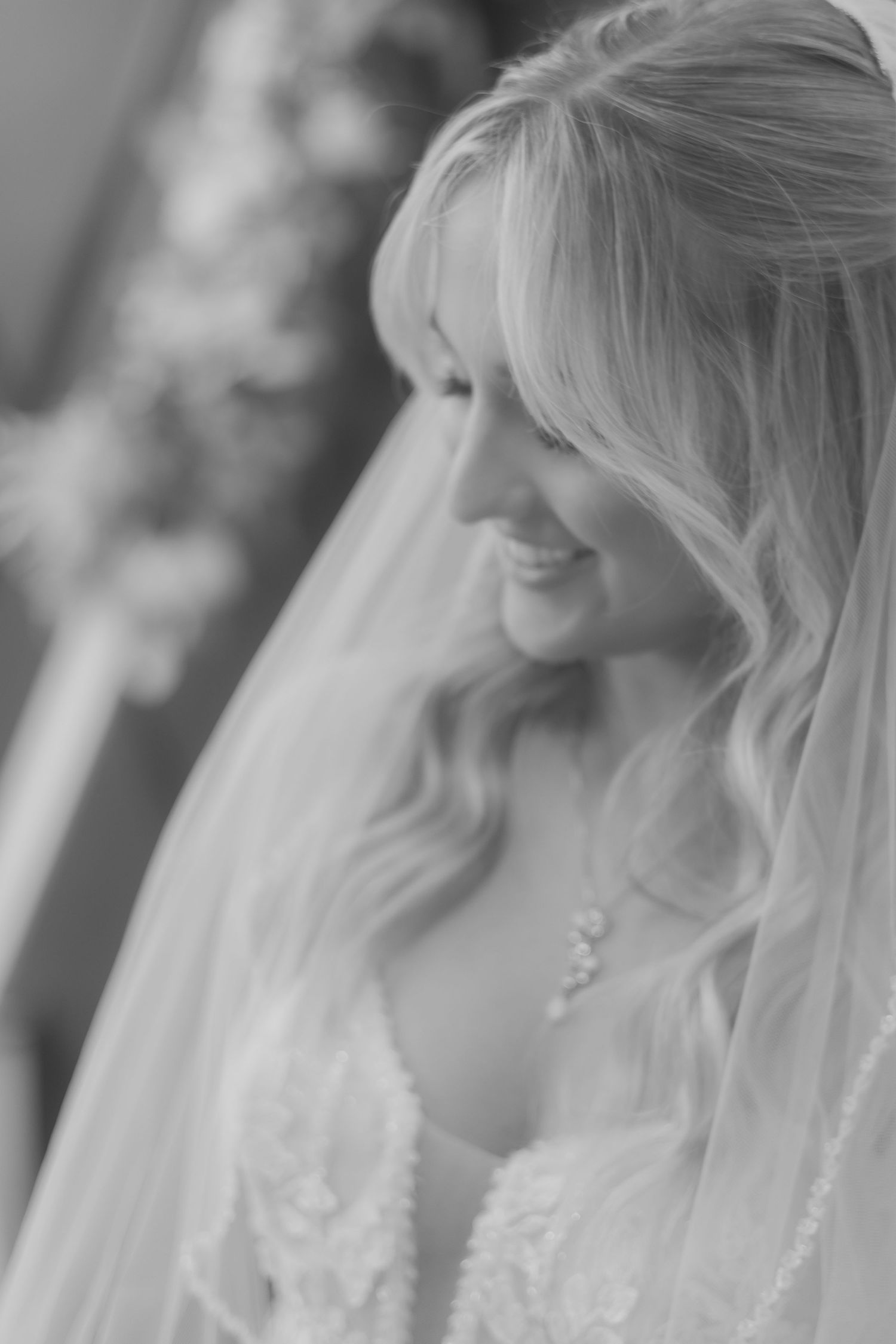 Beautiful blonde bride wearing a delicate veil and lace dress smiling on her wedding day.