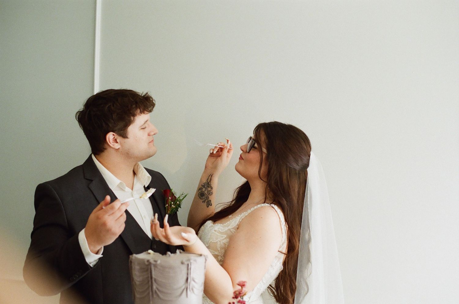 Bride and groom sharing a lighthearted cake tasting moment against a minimalist white background.