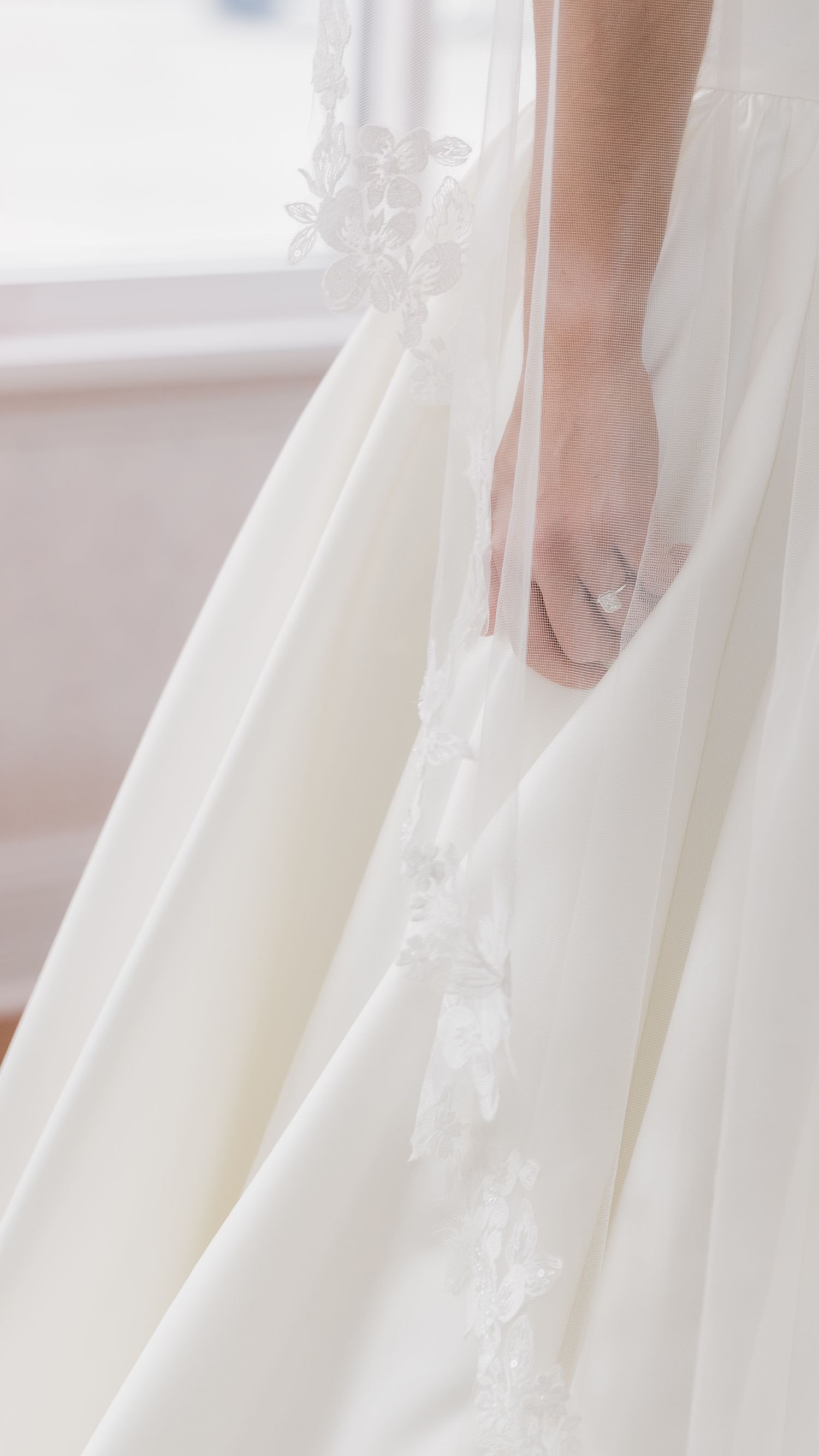 Bride holding her ivory satin wedding gown with delicate lace trim detail.