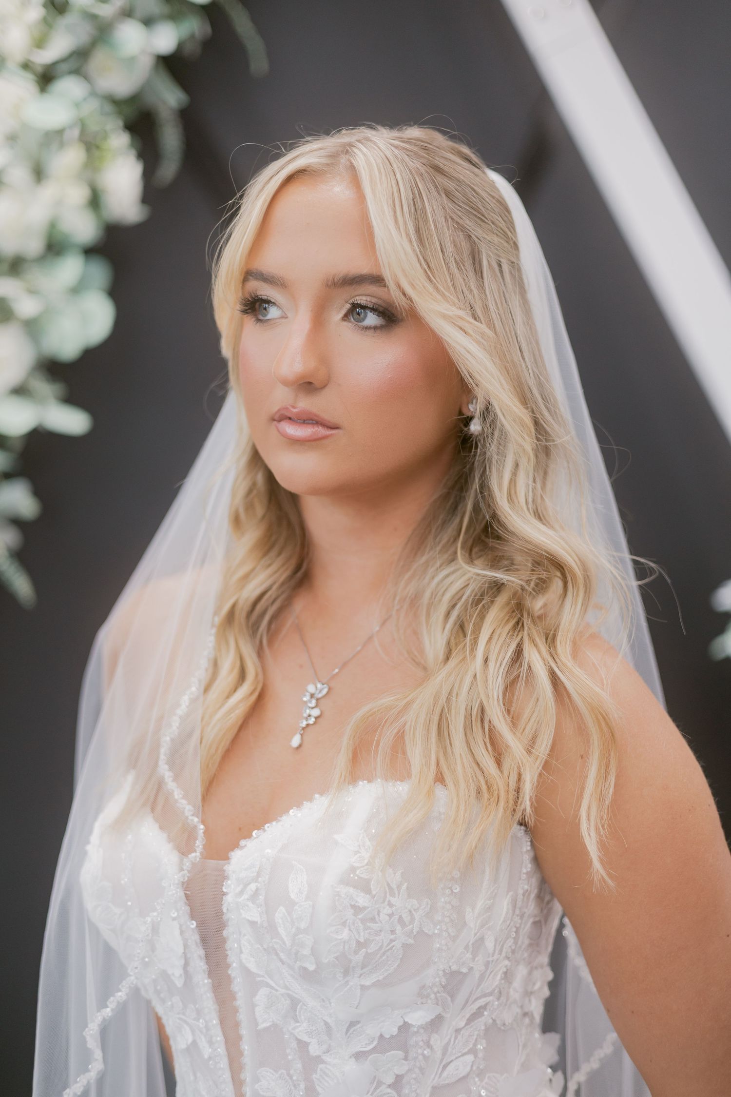 Close-up portrait of a blonde bride in a lace gown wearing a veil and delicate crystal drop necklace.
