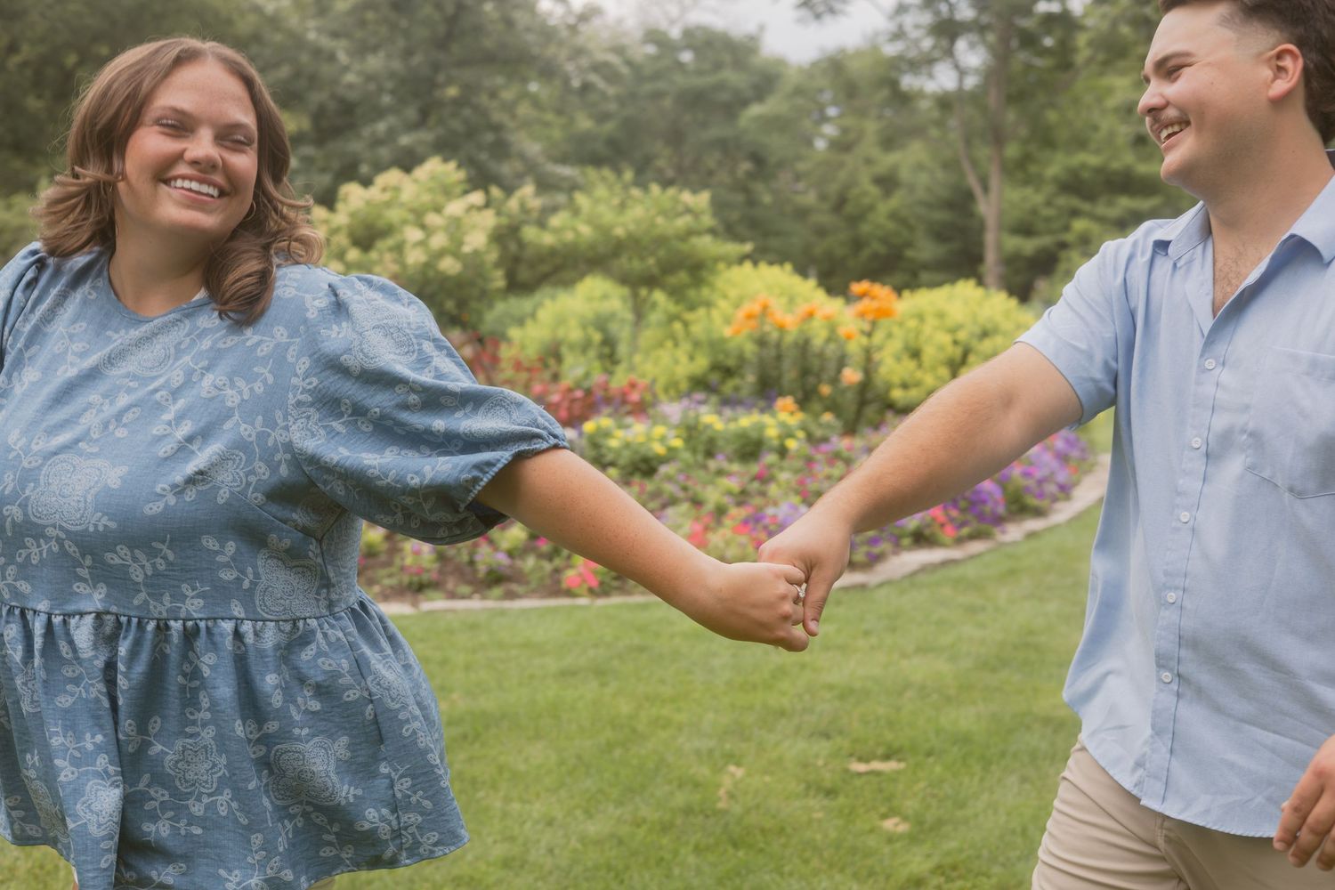 Happy couple holding hands and smiling while walking through a colorful blooming garden park.