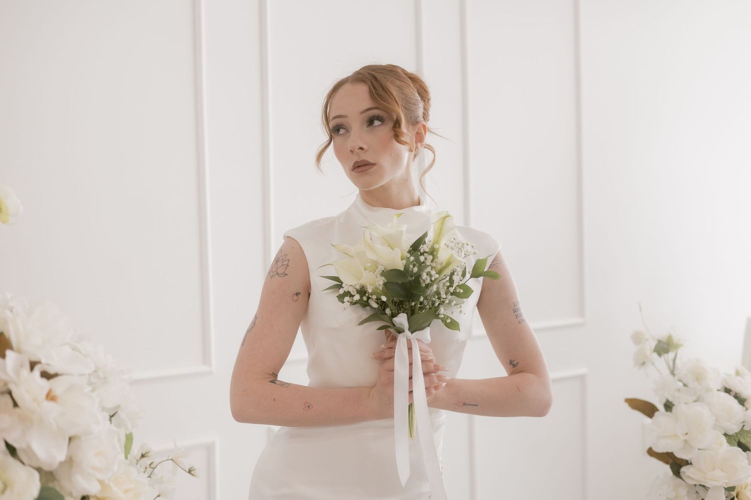 Young bride in white gown holding a white bouquet in a bright studio setting.