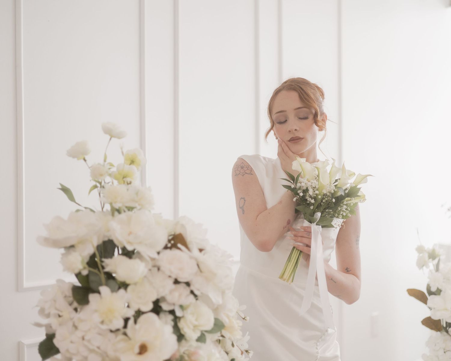 Elegant bride in white dress holding a bouquet of white flowers in a bright studio.