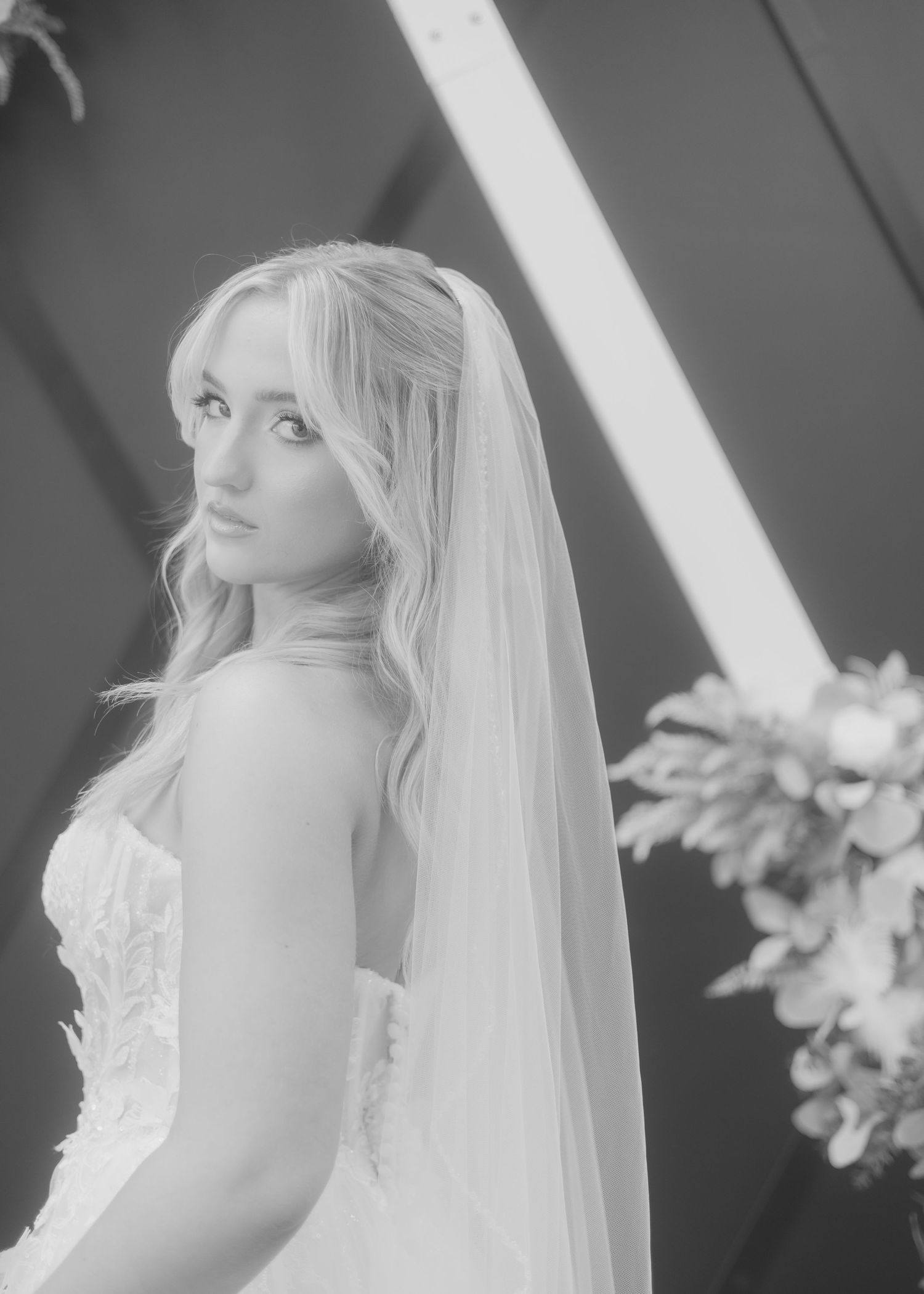 Black and white portrait of elegant blonde bride in strapless gown with long veil at altar.
