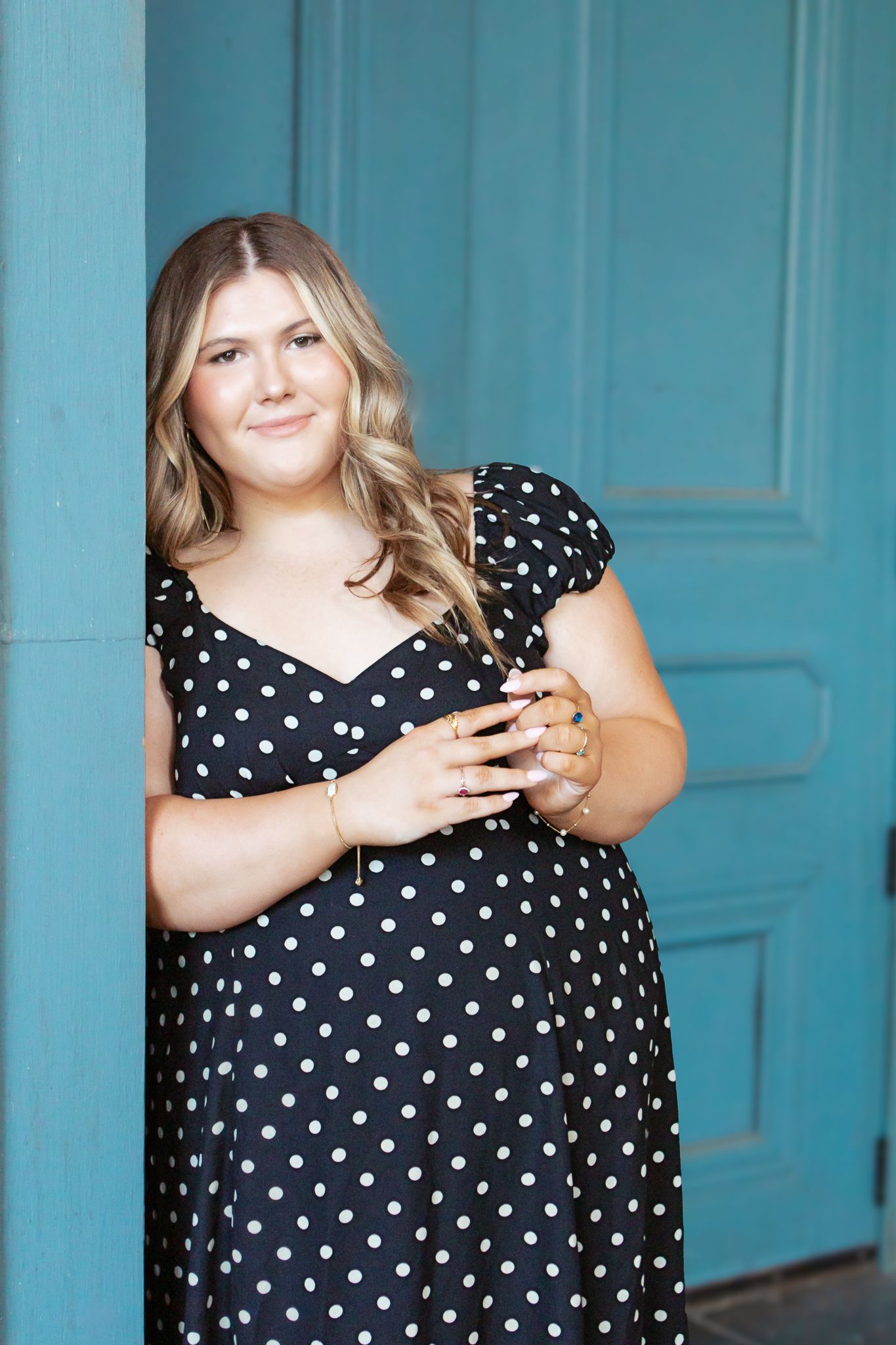 Young woman in black and white polka dot dress posing against a turquoise door.