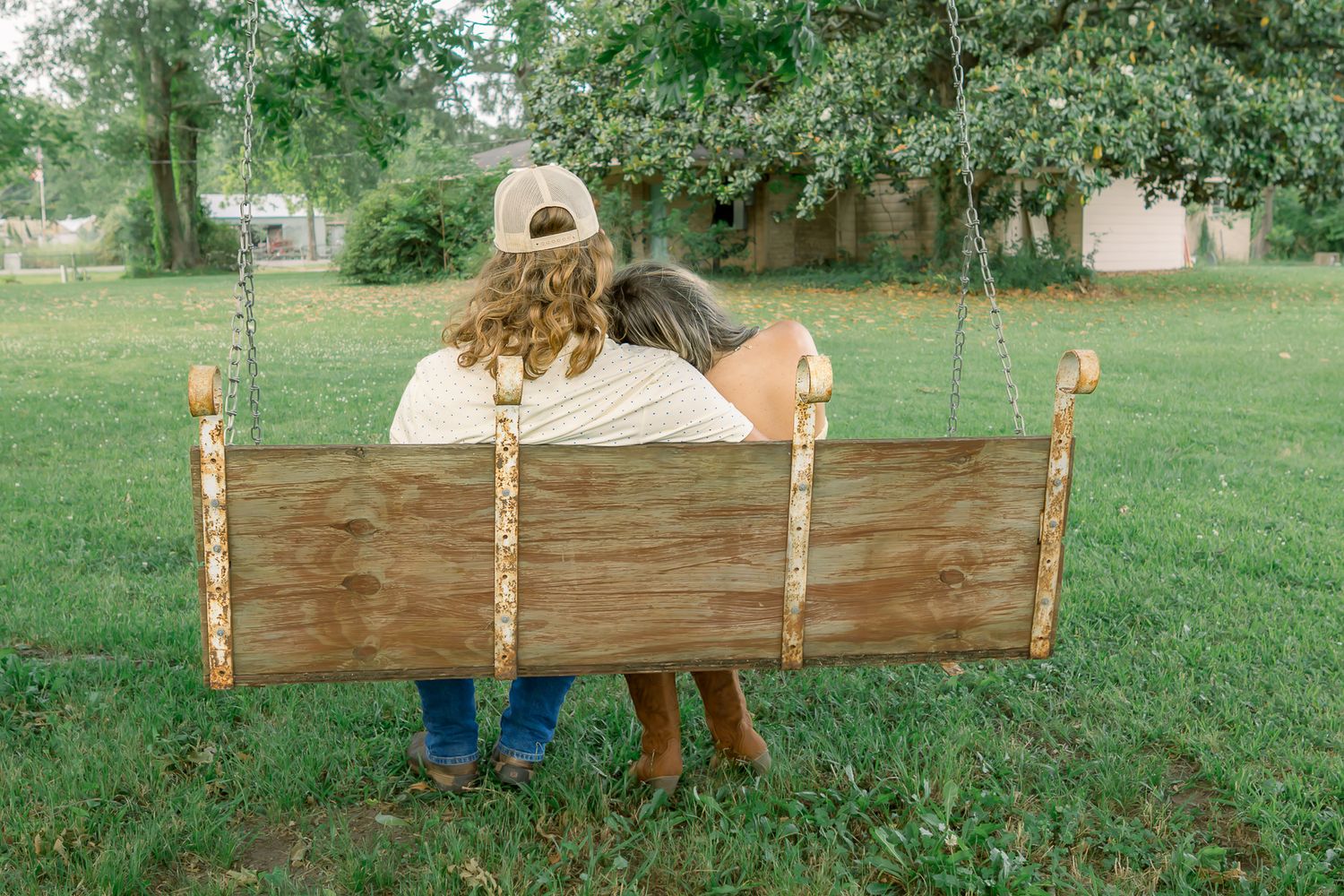 Couple sitting together on a wooden swing viewed from behind in a green yard.