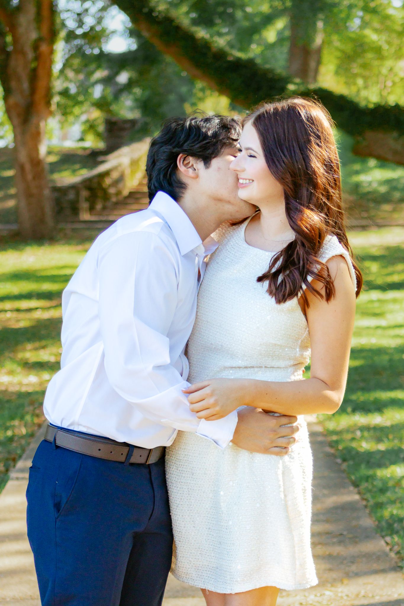 Couple sharing a romantic moment outdoors, man kissing woman's cheek in a park.