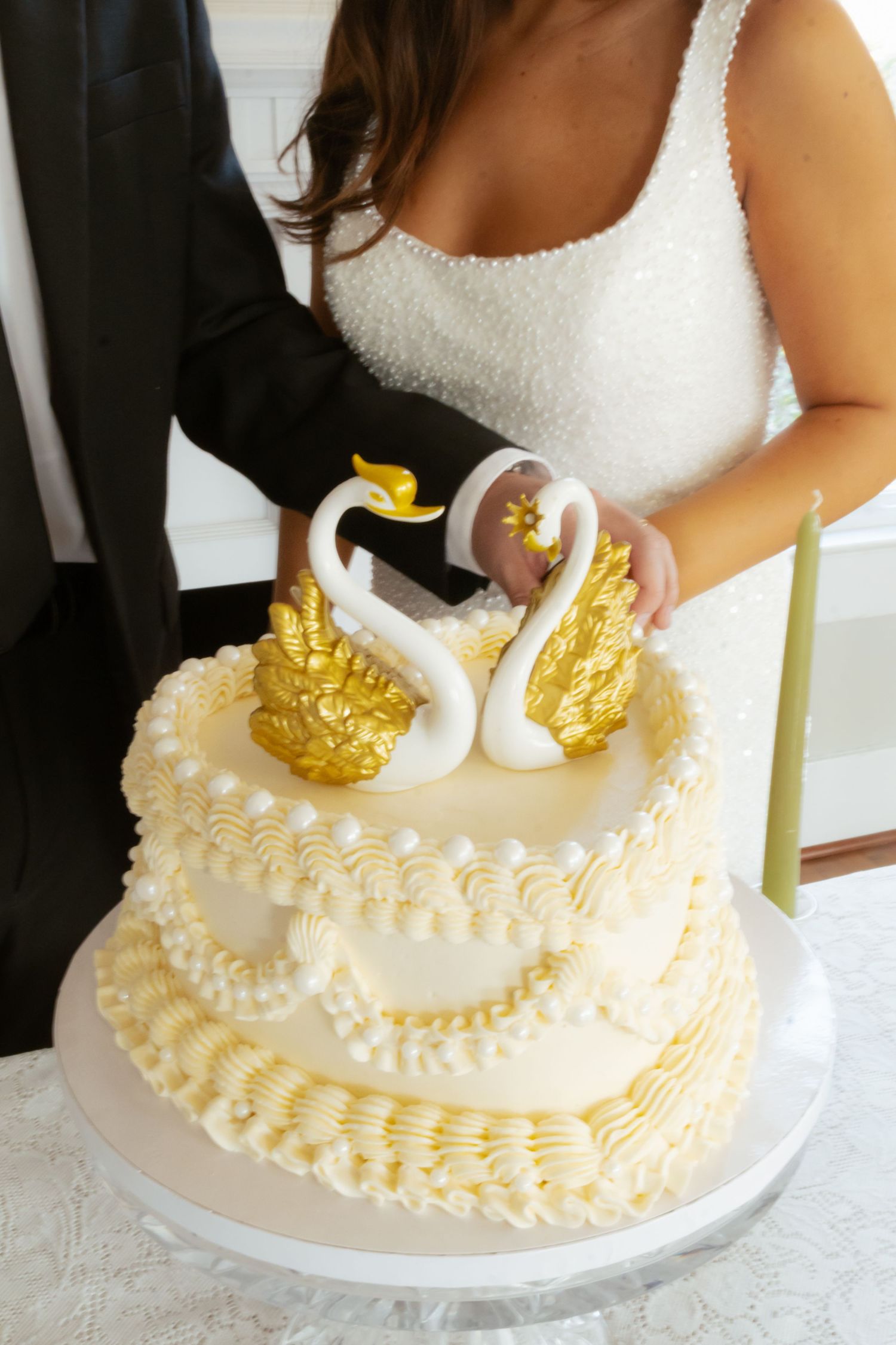 Bride and groom cutting elegant two-tier white wedding cake topped with gold and white swans.