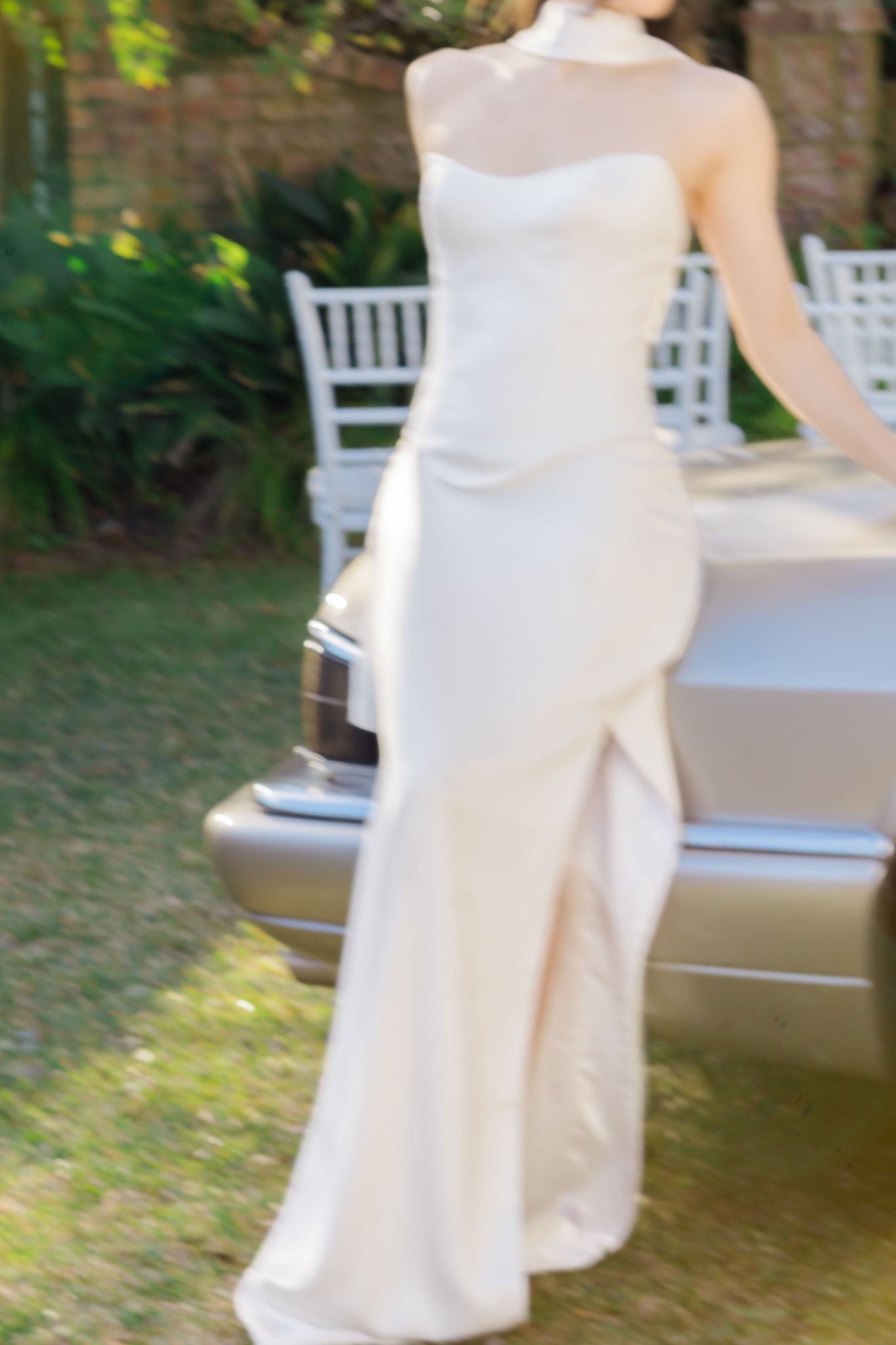 Elegant bride in a sleek ivory halter wedding gown standing beside a vintage silver car outdoors.