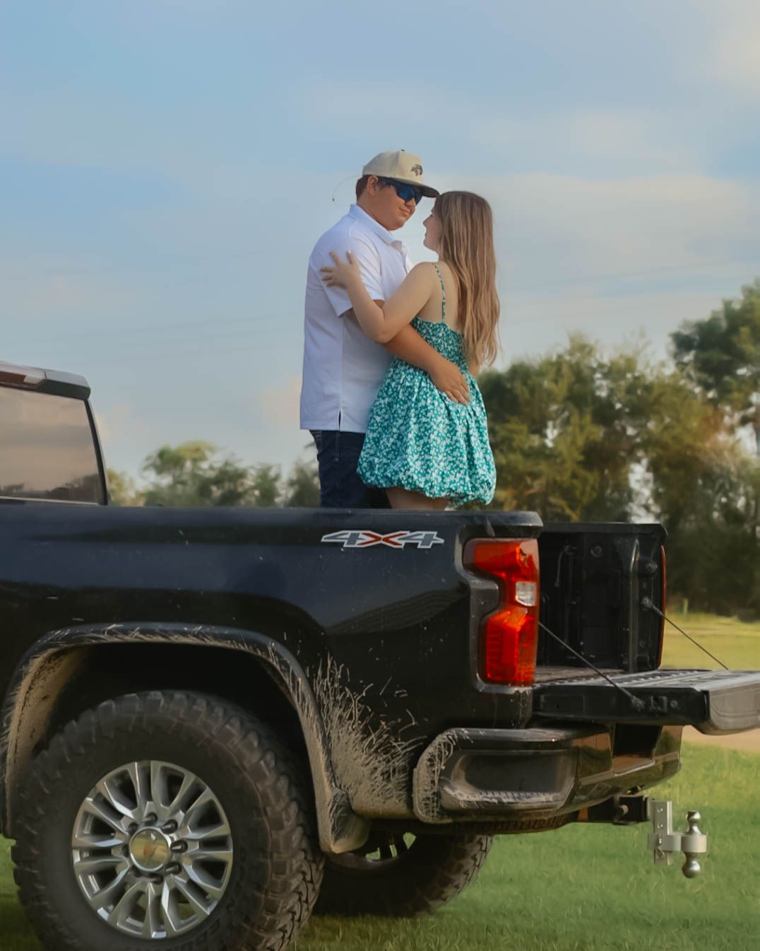 A couple sitting on the tailgate of a black pickup truck in an outdoor setting.