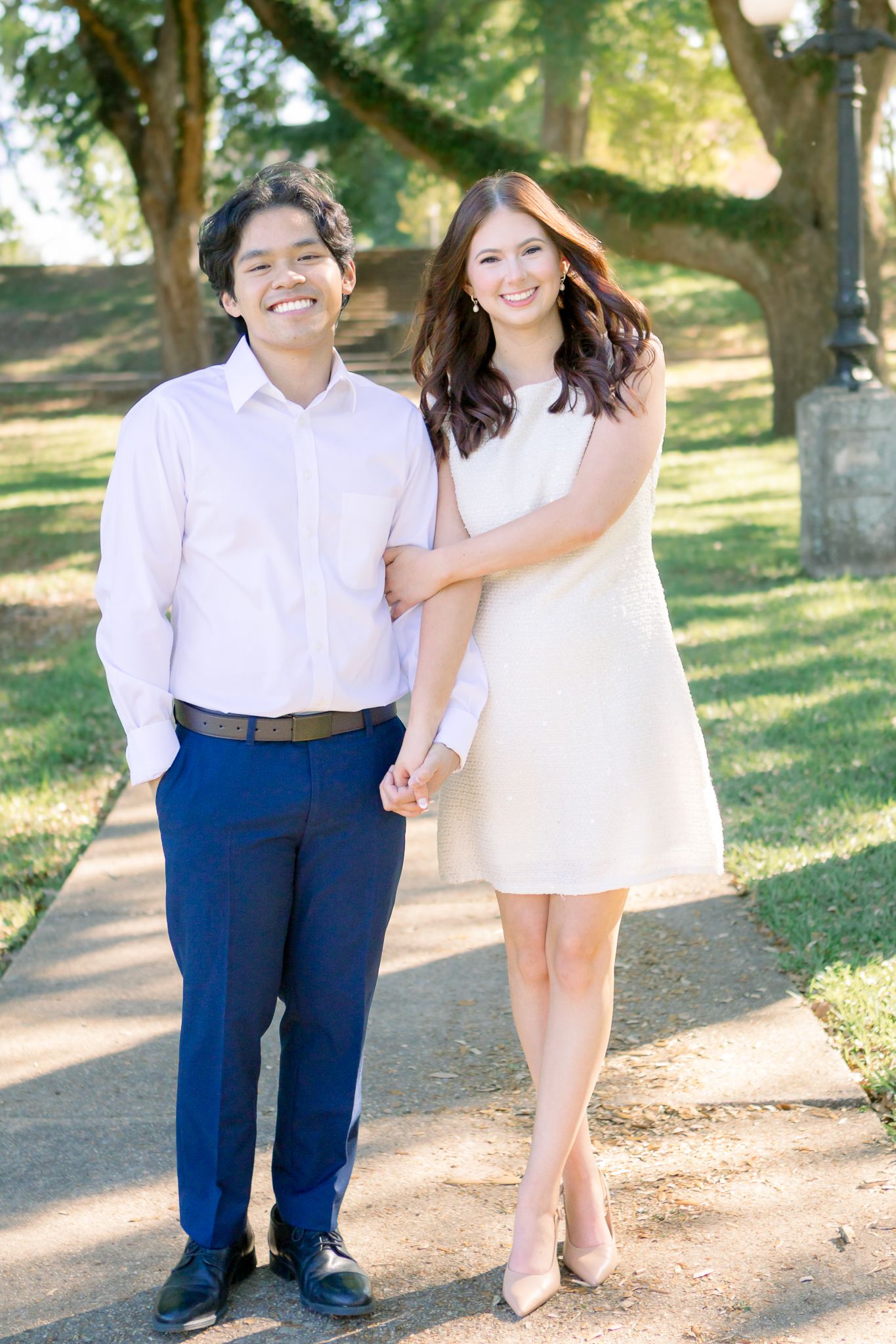 Smiling couple walking hand in hand on a sunny tree-lined path.