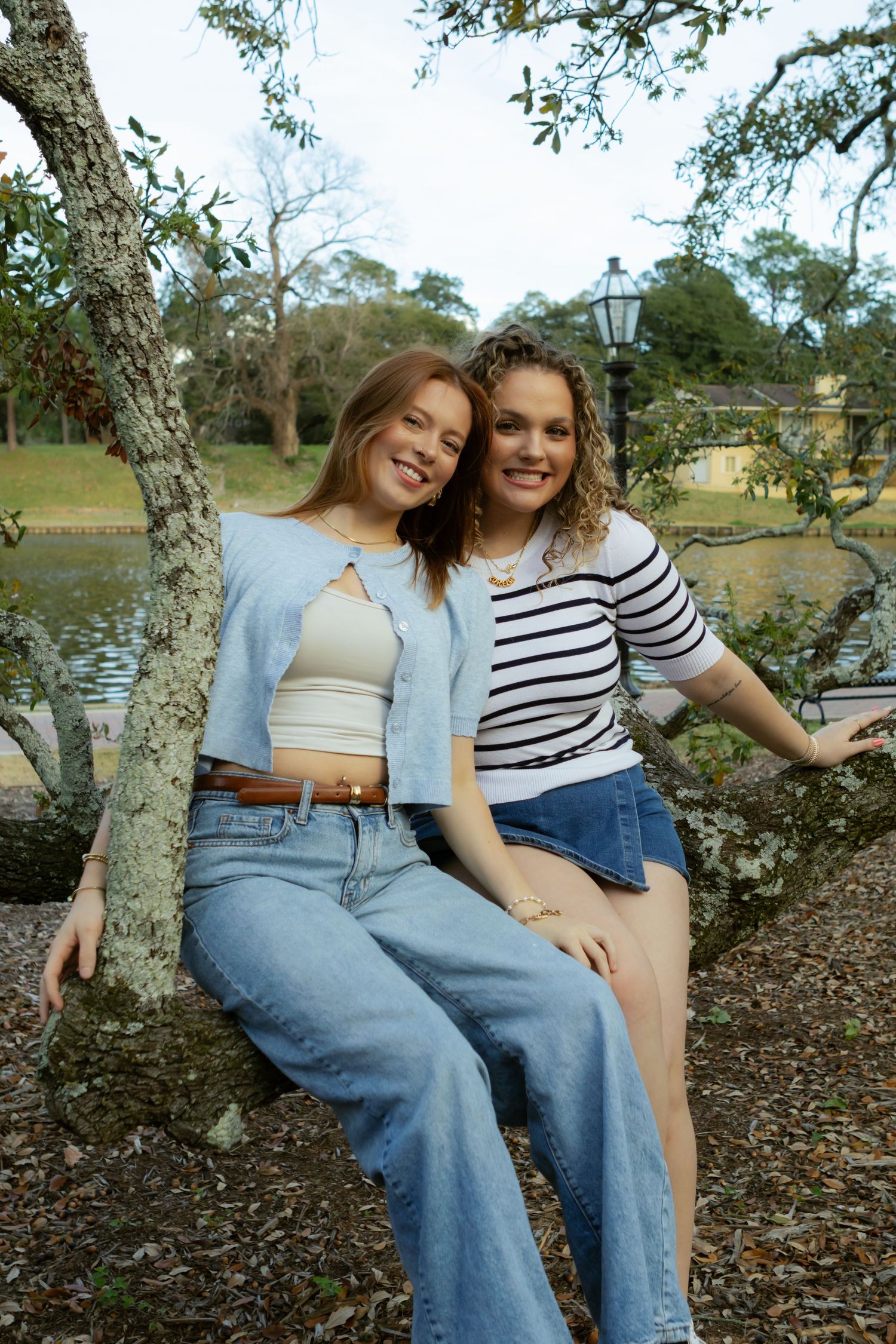 Two friends in casual denim outfits sitting together on a tree branch on a sunny autumn day.
