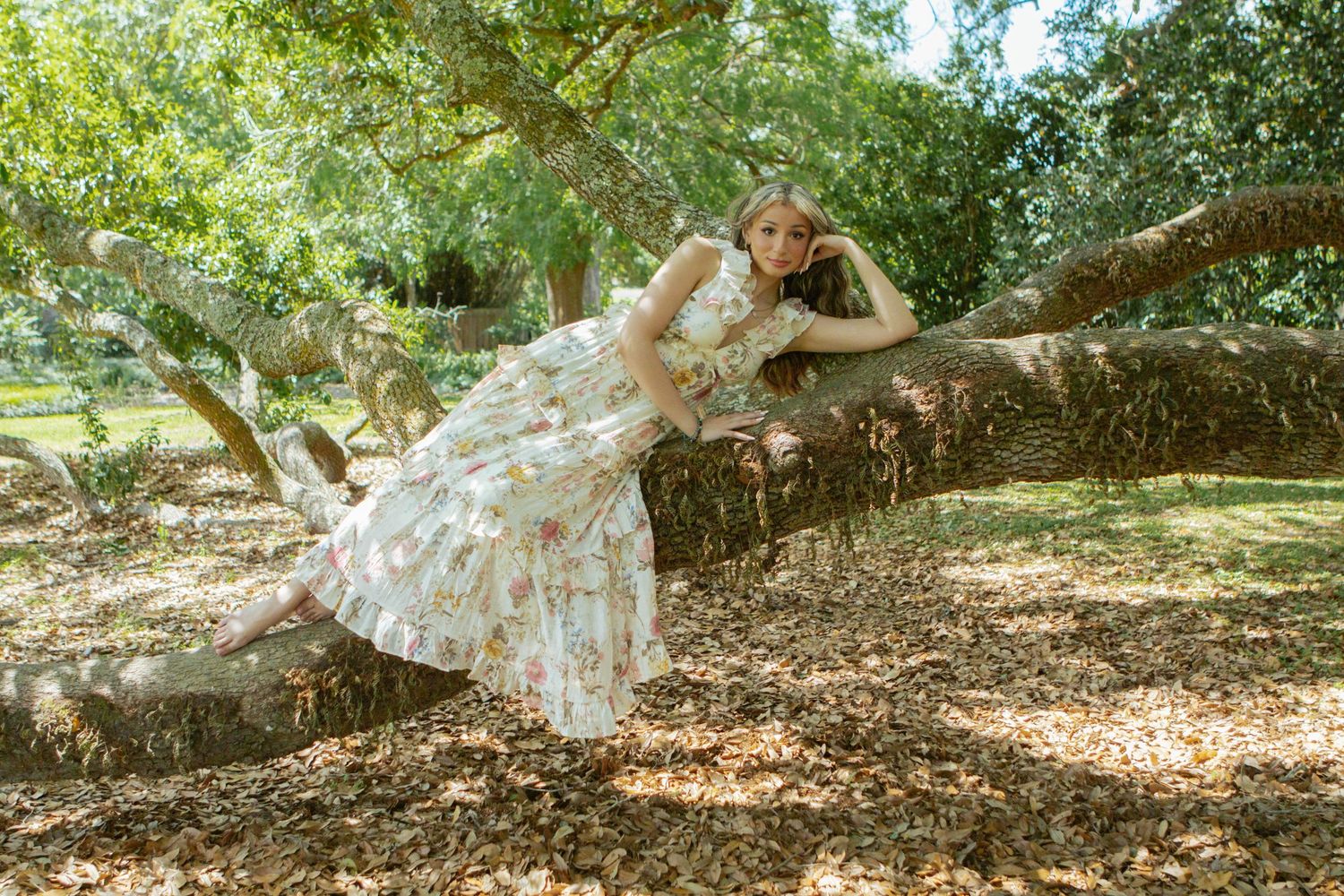 Young woman in floral dress reclining on a large tree branch in a park.