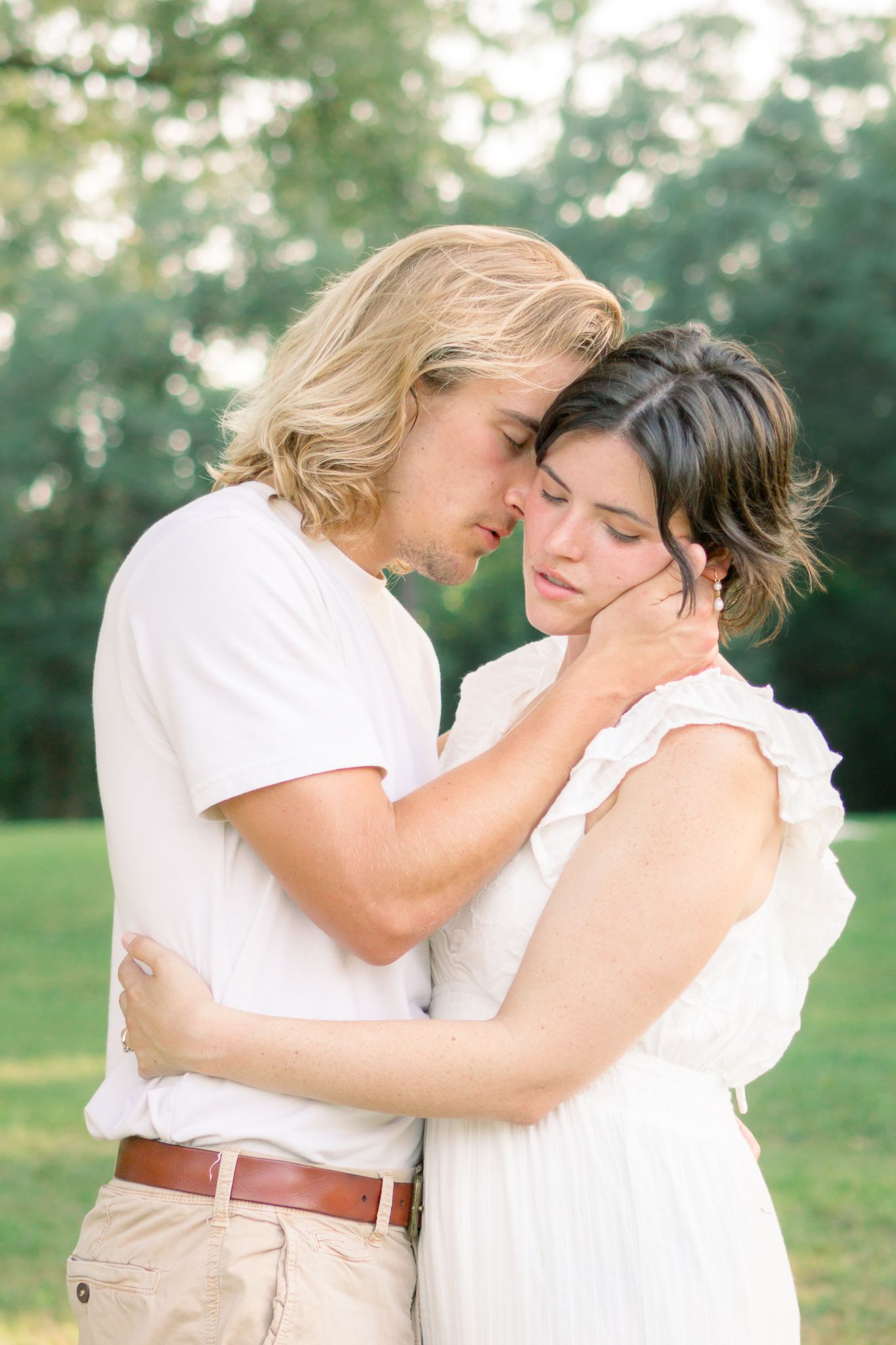 A couple in white clothing share a tender embrace outdoors, with the man gently cradling the woman's face.