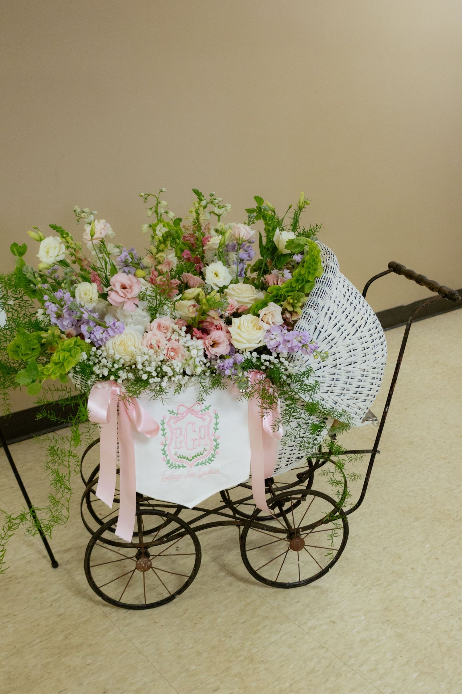 Vintage white wicker baby carriage filled with pink and white floral arrangement with pink ribbons.
