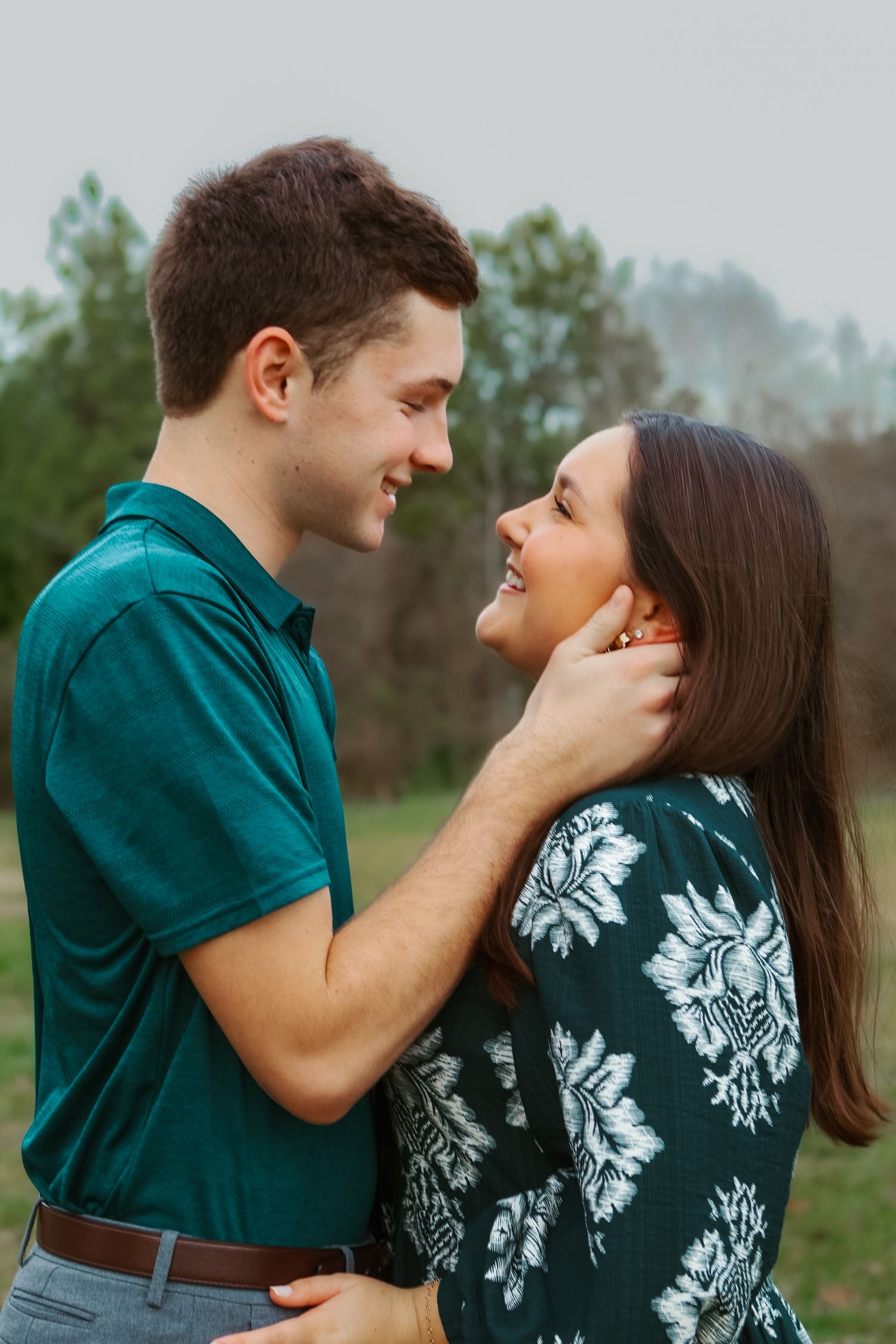 A couple in coordinated outfits share a tender romantic moment outdoors in a natural setting.