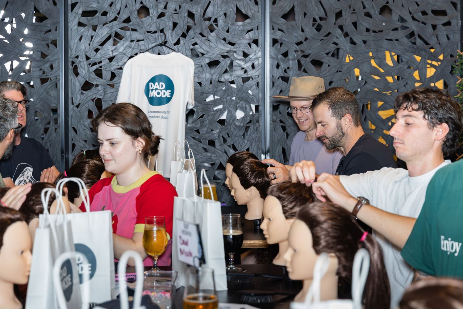 People practice hairstyling on mannequin heads at a hair styling workshop event with Mad Mode branding.