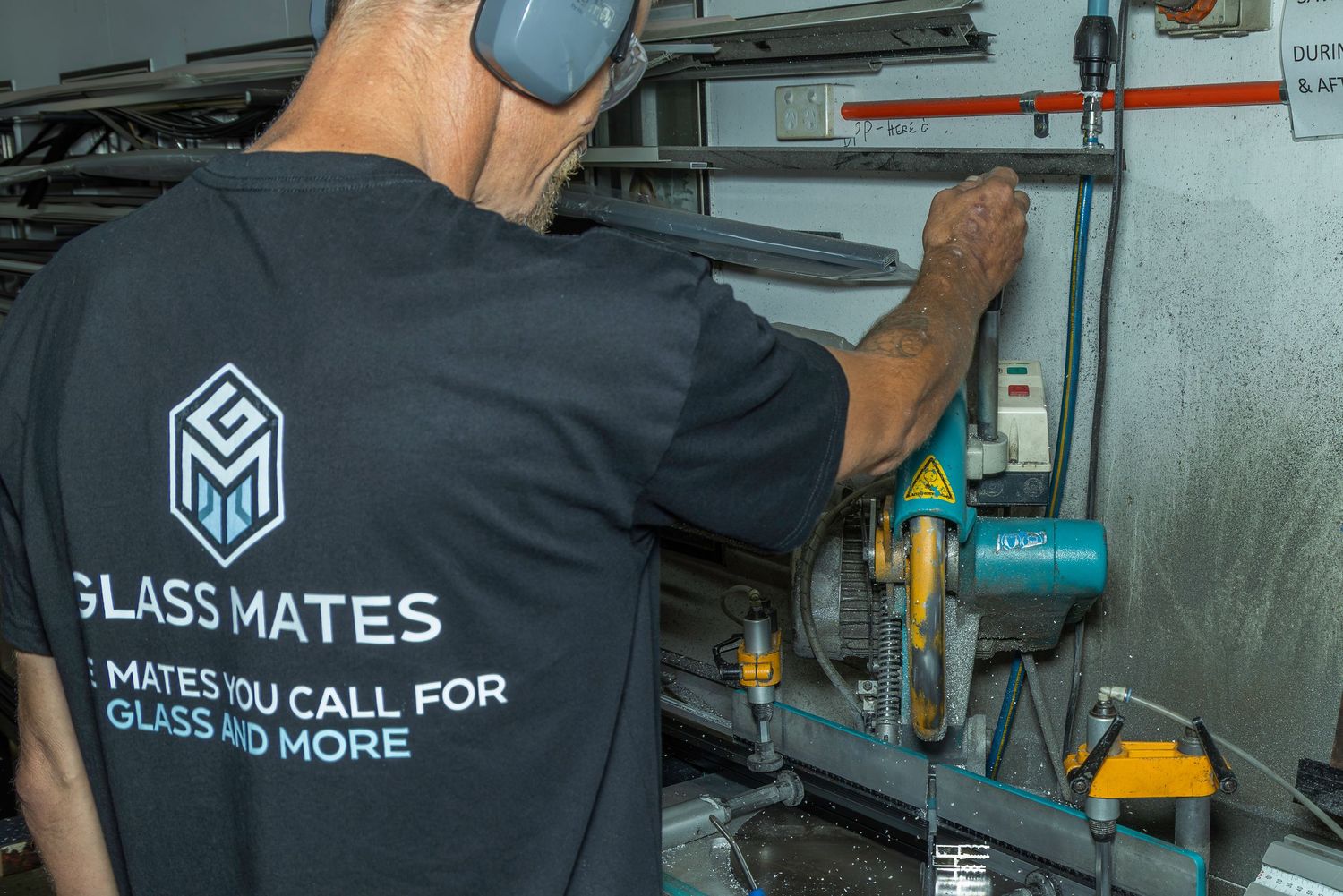 Glass Mates technician in branded black t-shirt operating glass cutting equipment in a professional workshop.