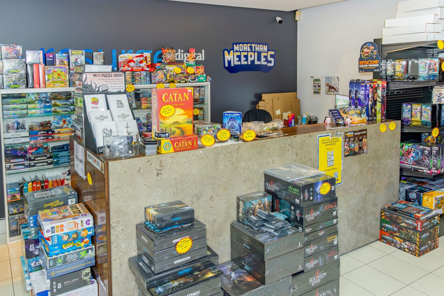 Interior of More Than Meeples board game store with Catan and other games displayed on shelves and counter.