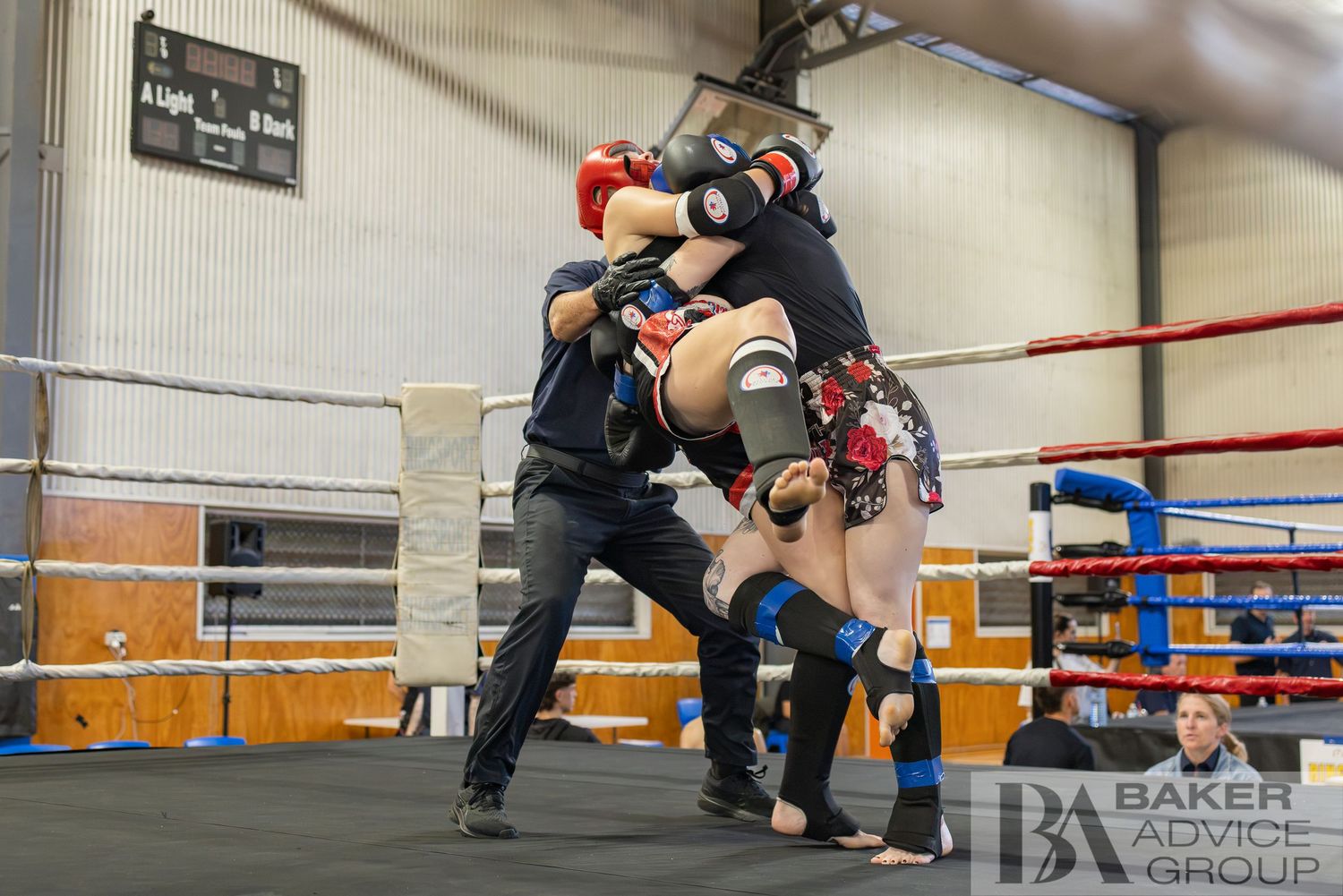 Two fighters clinch during an intense kickboxing bout inside a boxing ring with a referee watching closely.