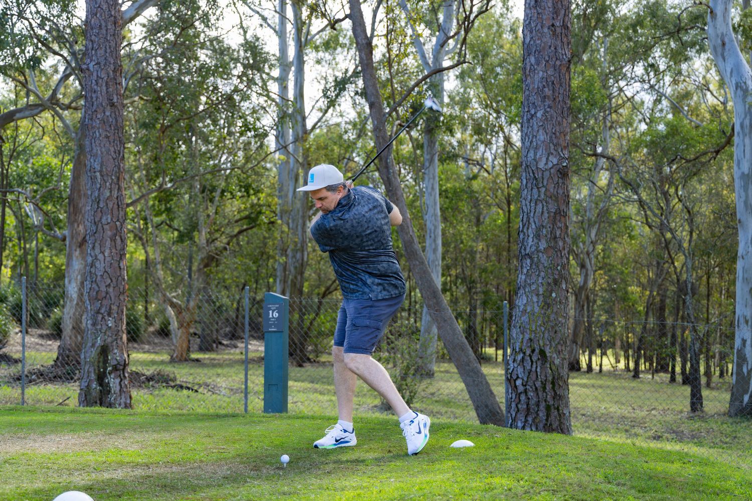 Male golfer finishing a tee shot swing between tall trees on an Australian bush golf course.