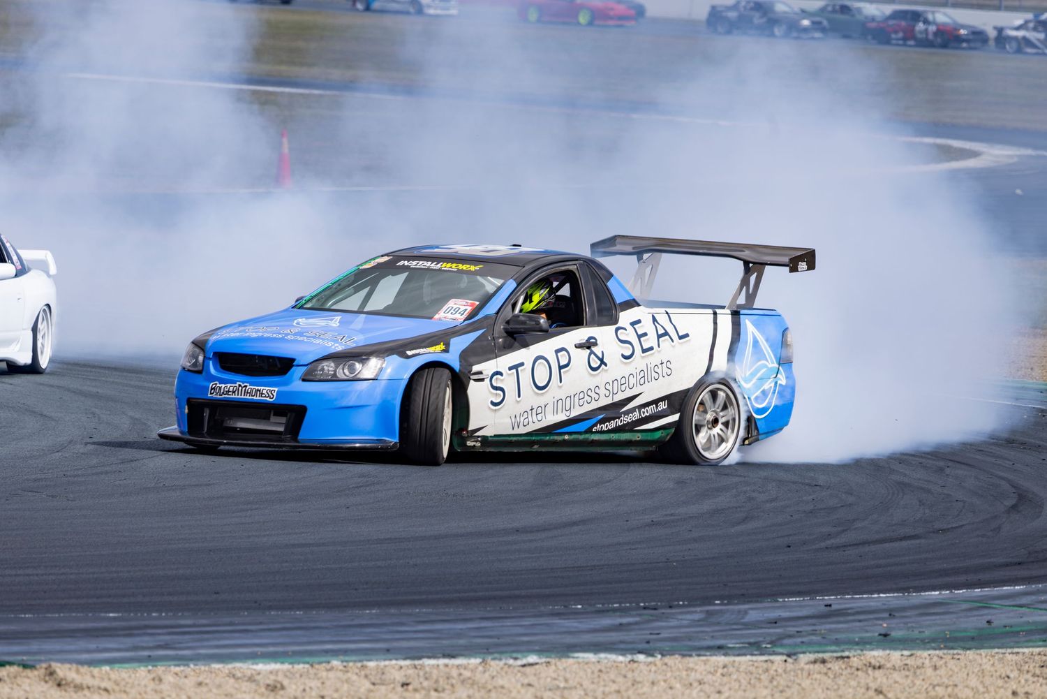 Blue Stop & Seal sponsored drift car producing smoke on a racing circuit during a competitive drifting event.