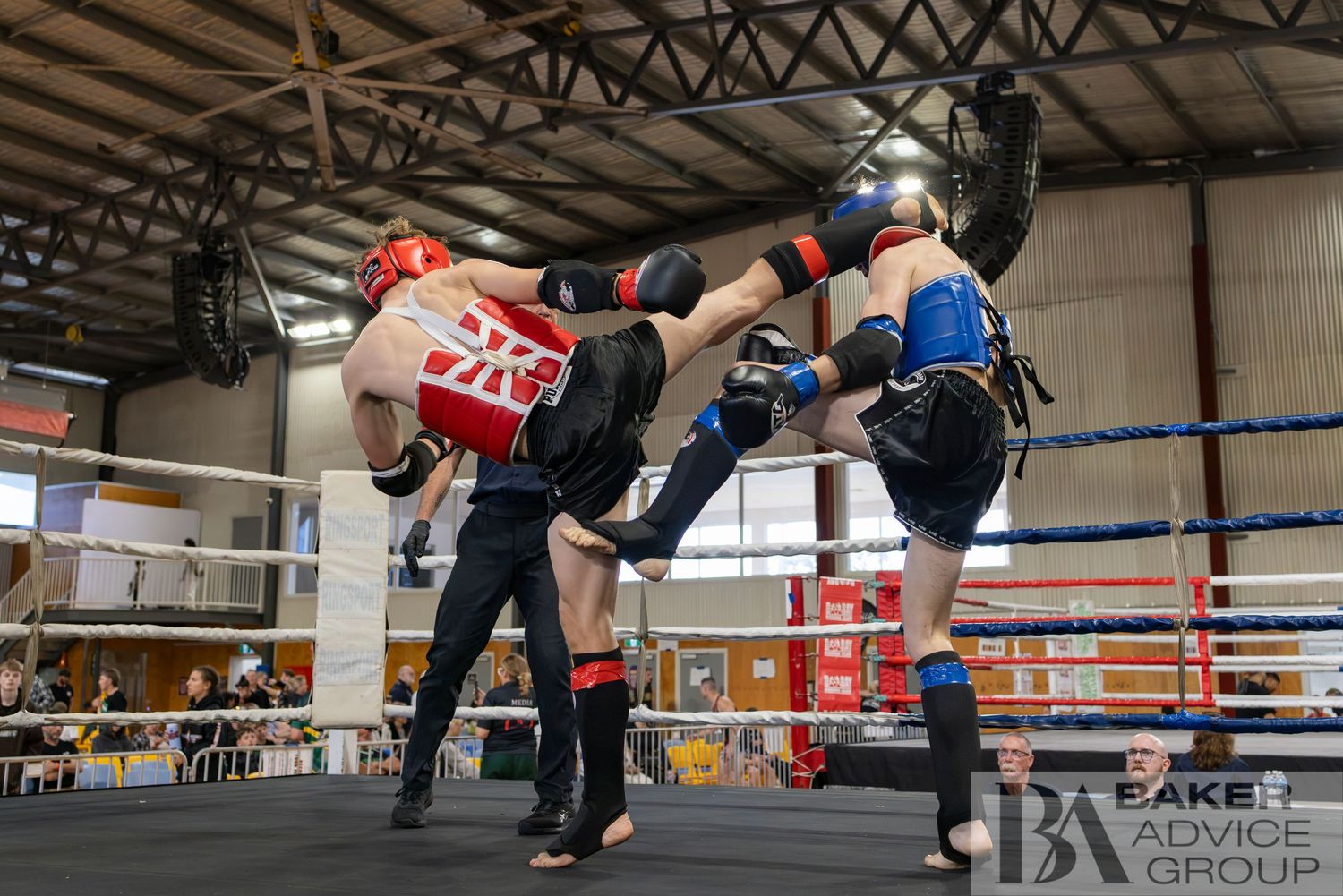 Two kickboxers sparring in a ring, one executing a high kick while wearing red and blue protective gear.