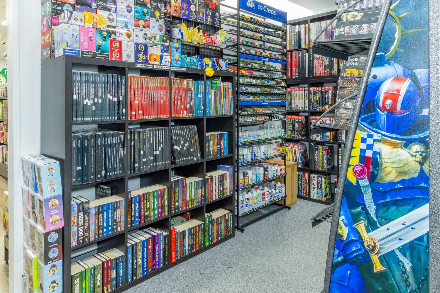 Retail store shelves stocked with video games, DVDs, and board games in organized rows with an arcade machine visible.