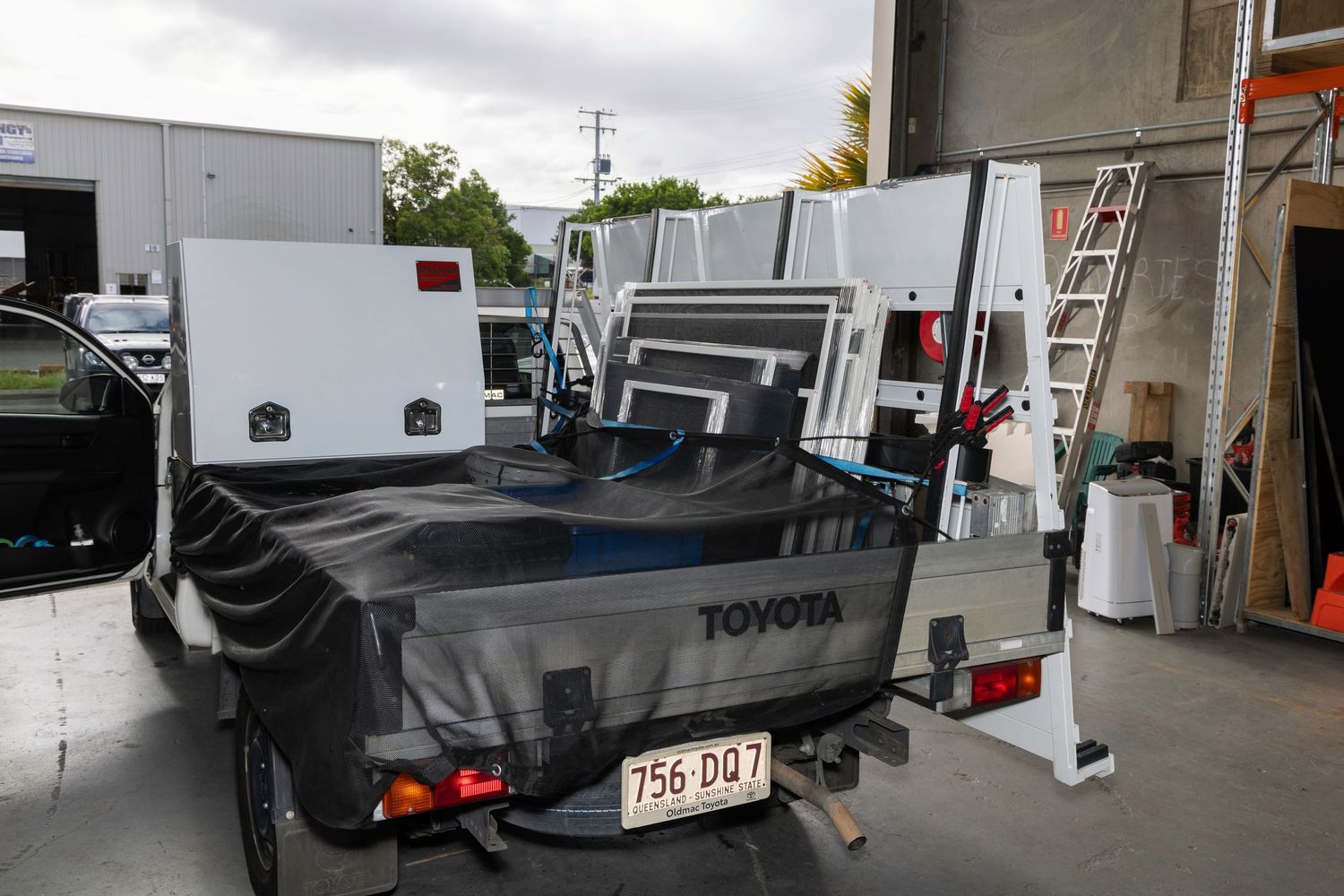 Toyota truck bed loaded with white toolboxes and equipment parked outside an industrial workshop.