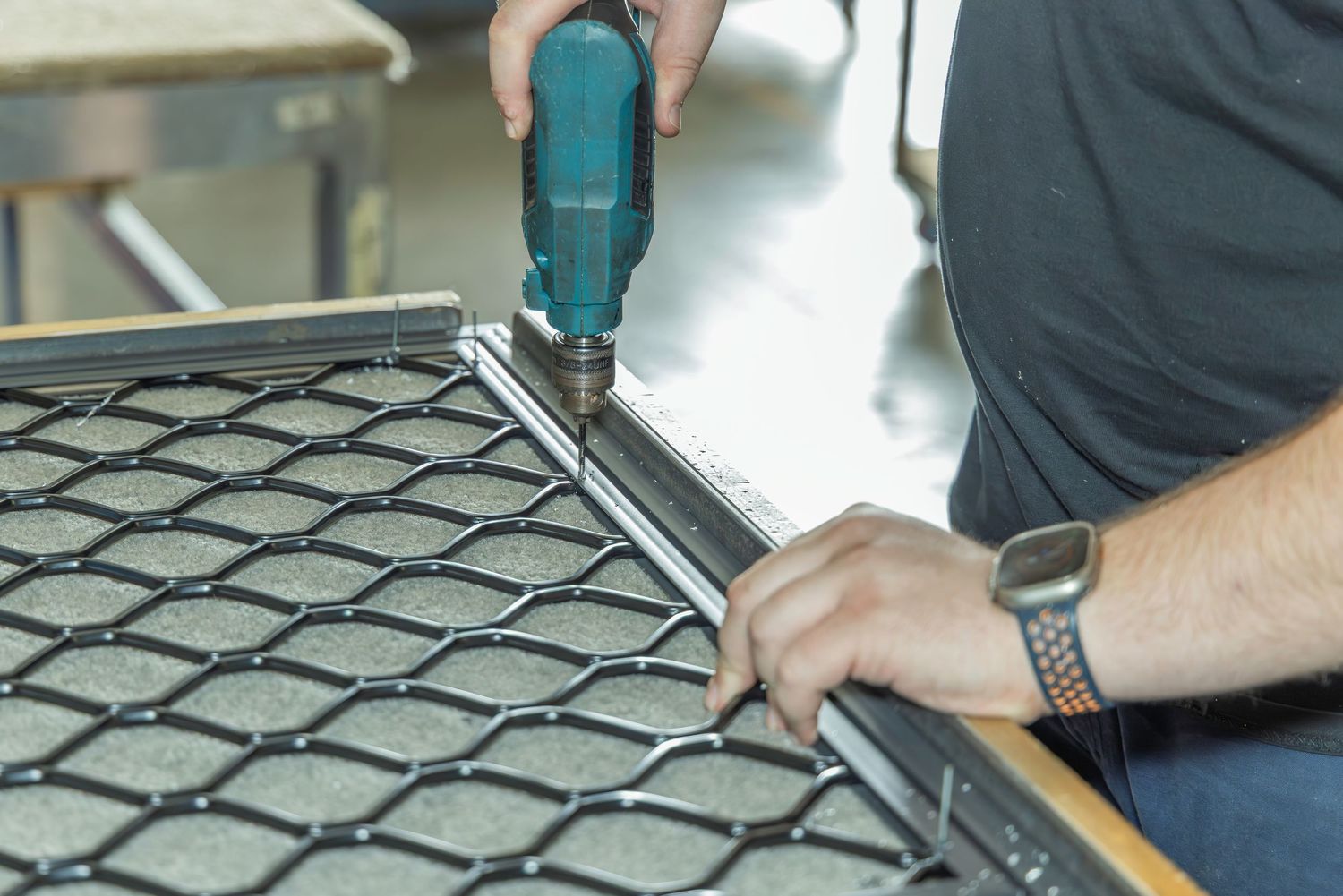 Technician using a Makita drill to assemble a metal mesh grid frame in a workshop setting.