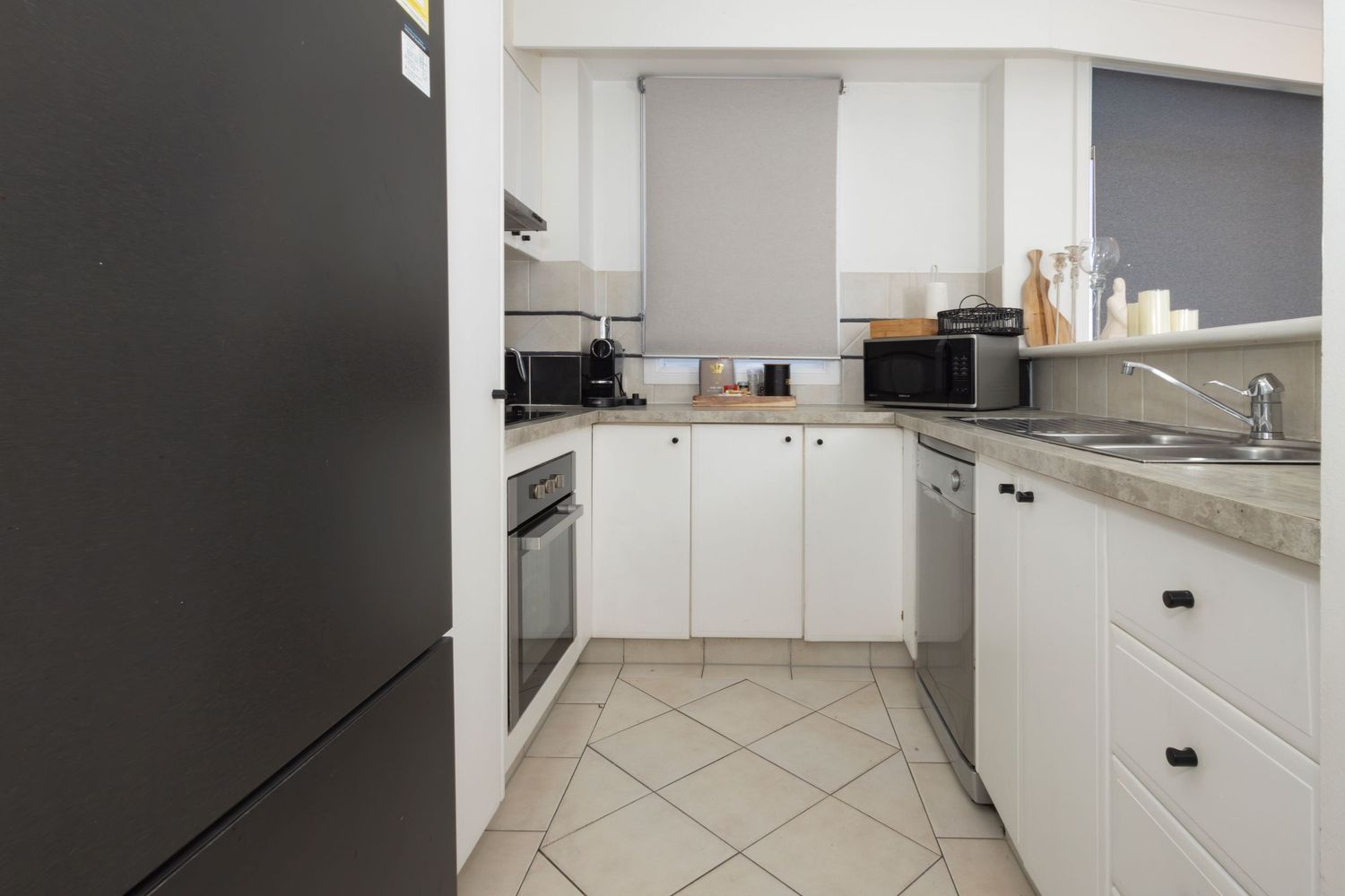 Modern U-shaped kitchen with white cabinets, black refrigerator, stainless steel oven, and tile flooring.