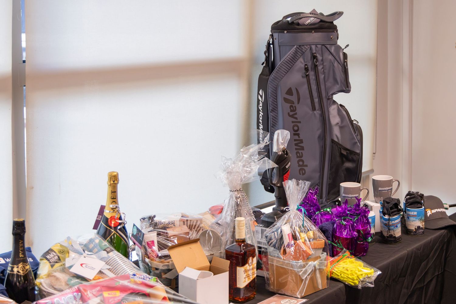 Golf bag and prize table with champagne, snacks, and gifts at a charity or corporate golf tournament event.