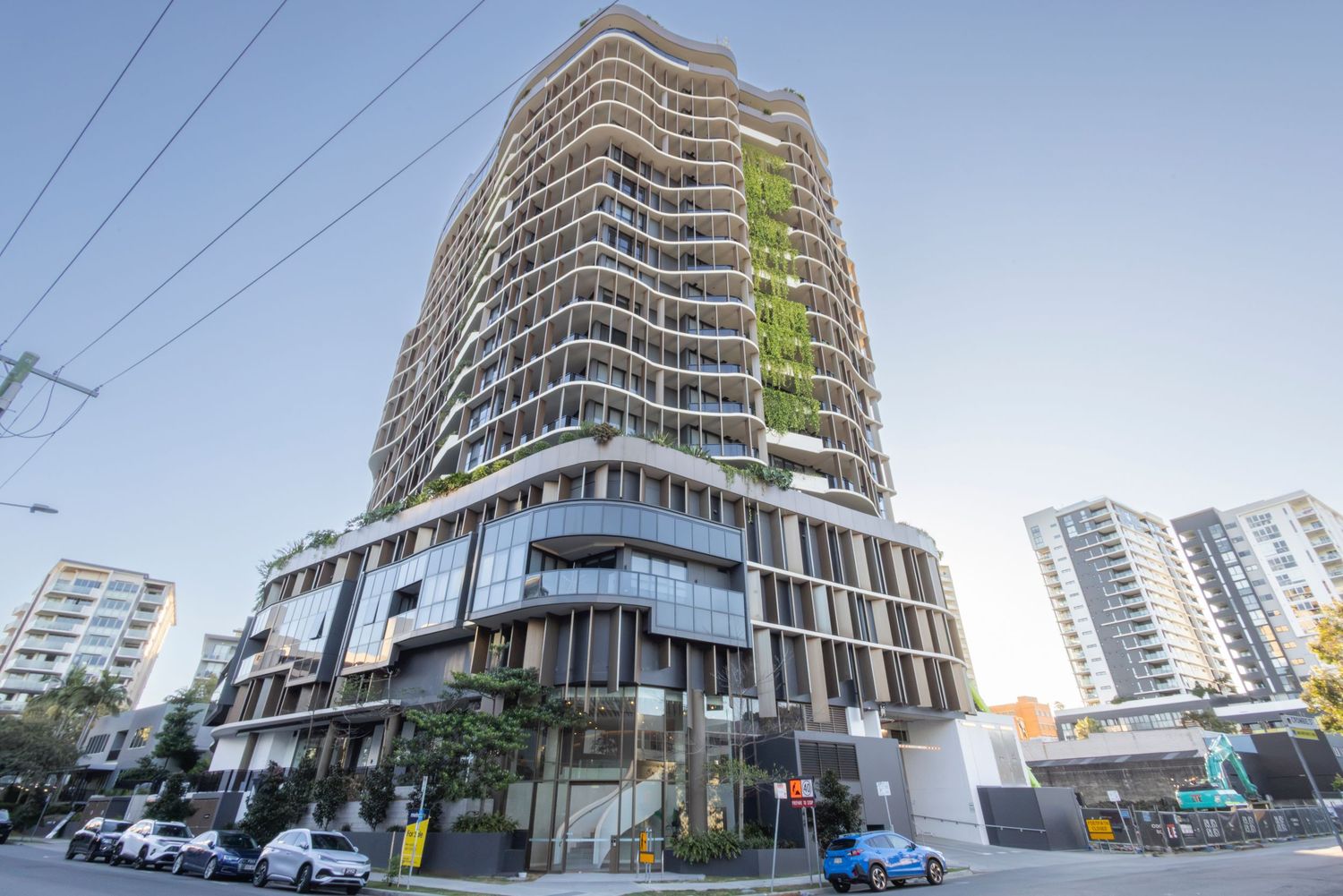 Tall contemporary residential tower with wavy facade and green terraces in urban setting.