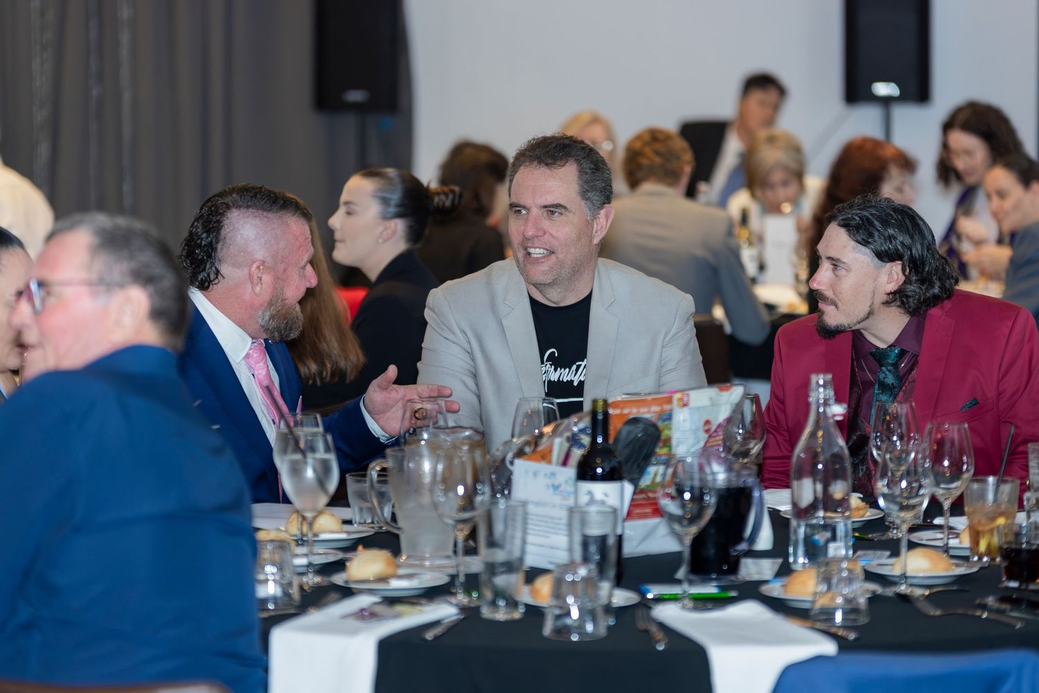 Guests networking and laughing at a formal banquet dinner event with elegantly set tables and wine glasses.