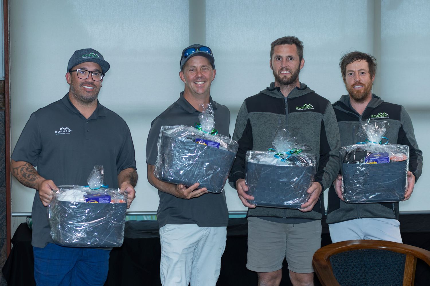 Four men smiling and holding gift baskets at an awards event or golf tournament prize ceremony.