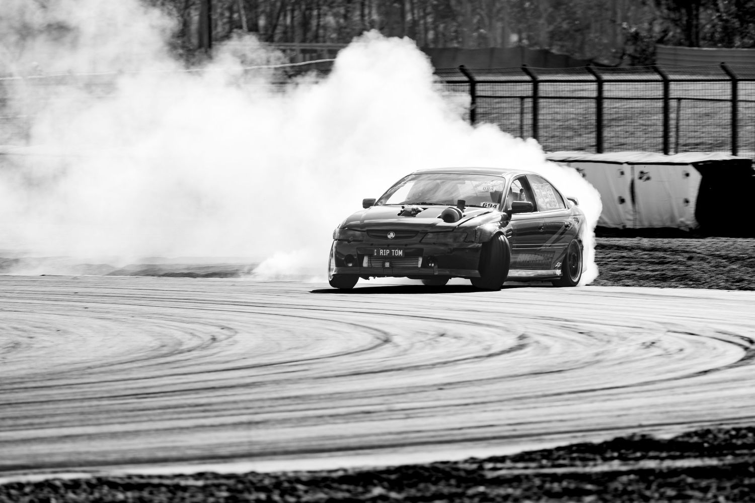 A car drifting on a racetrack with dramatic tire smoke in black and white.
