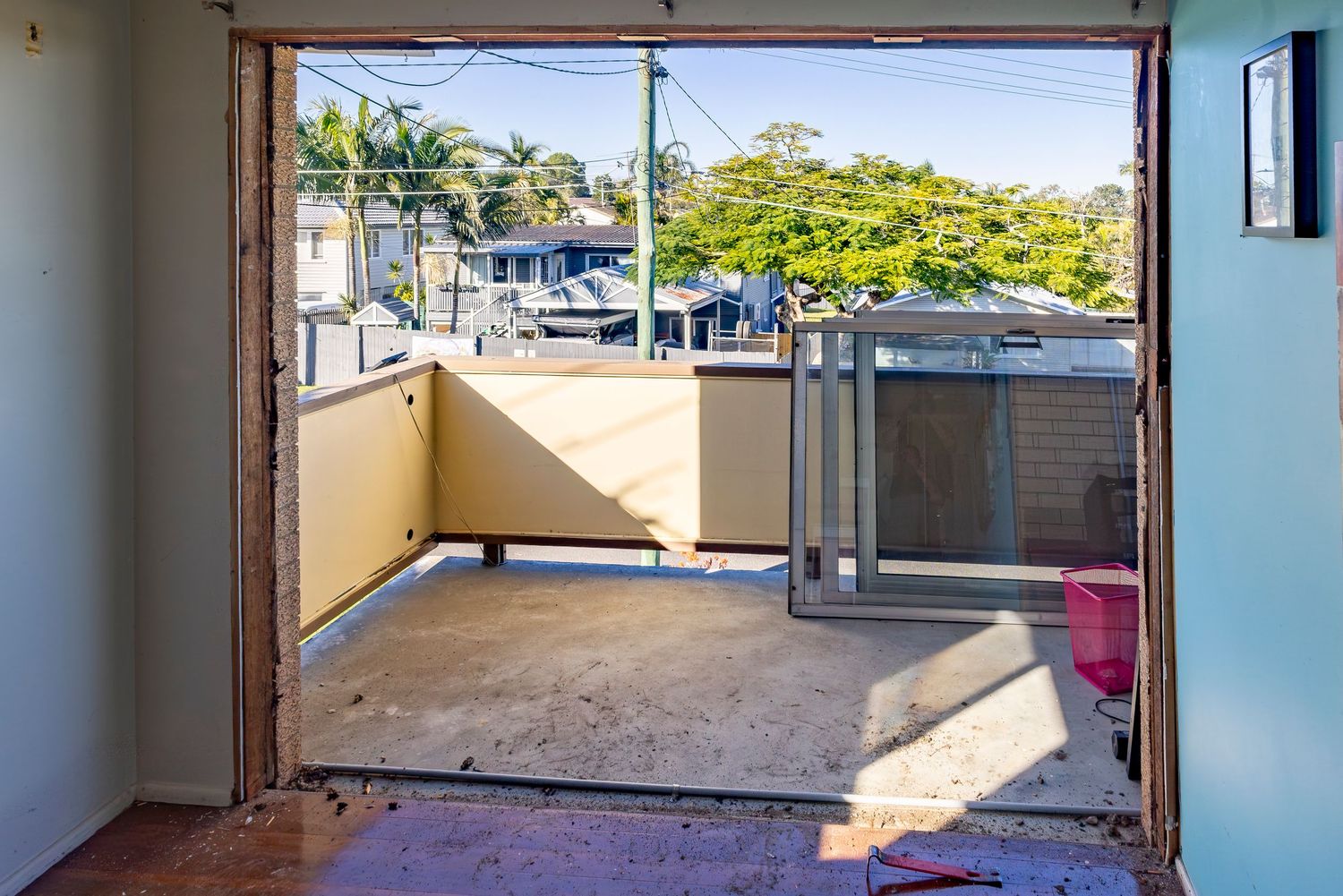 Open doorway leading to a small balcony with yellow walls, concrete floor, and tree views on a sunny day.