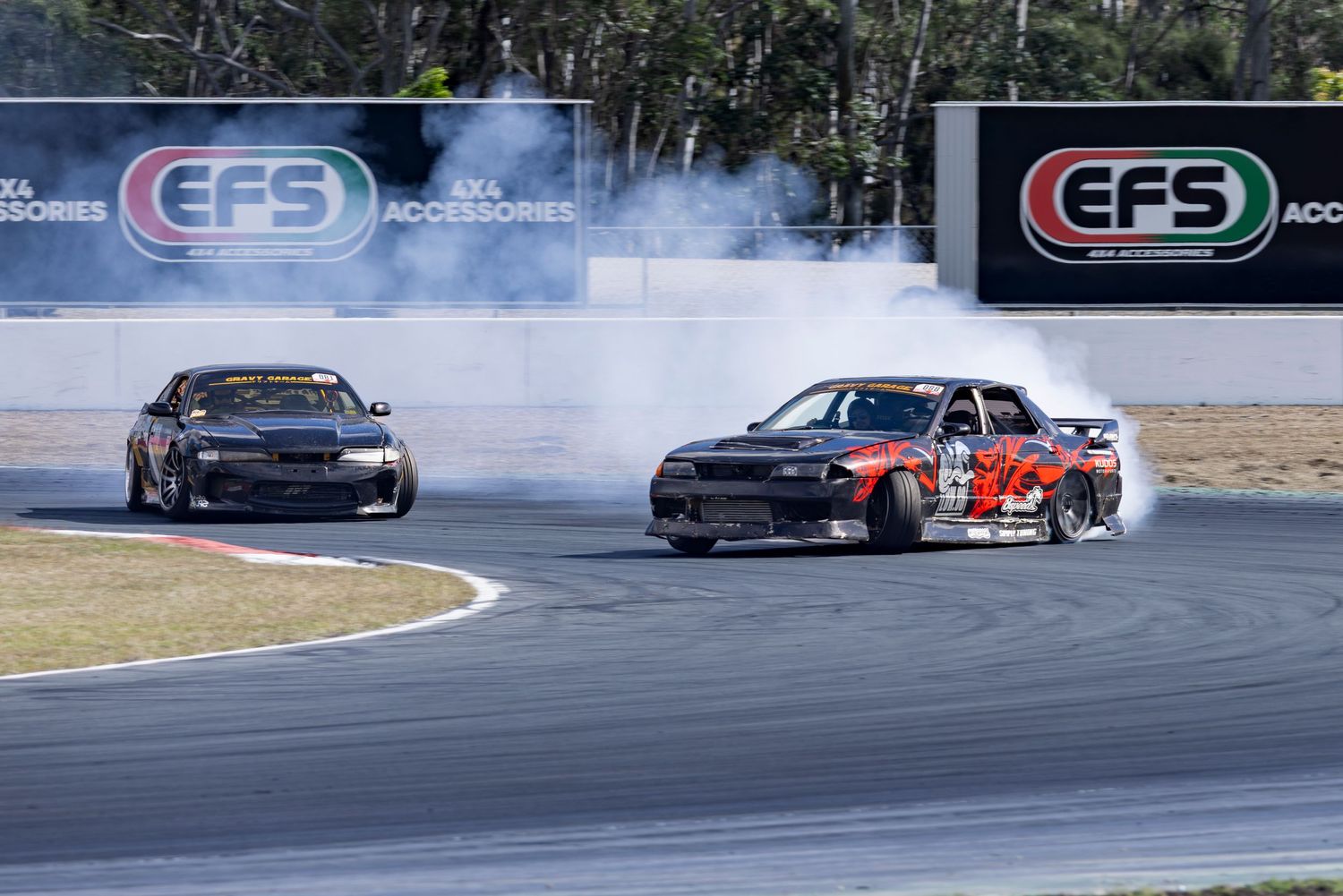 Two cars drifting around a corner on a race track with EFS sponsor banners visible in background.