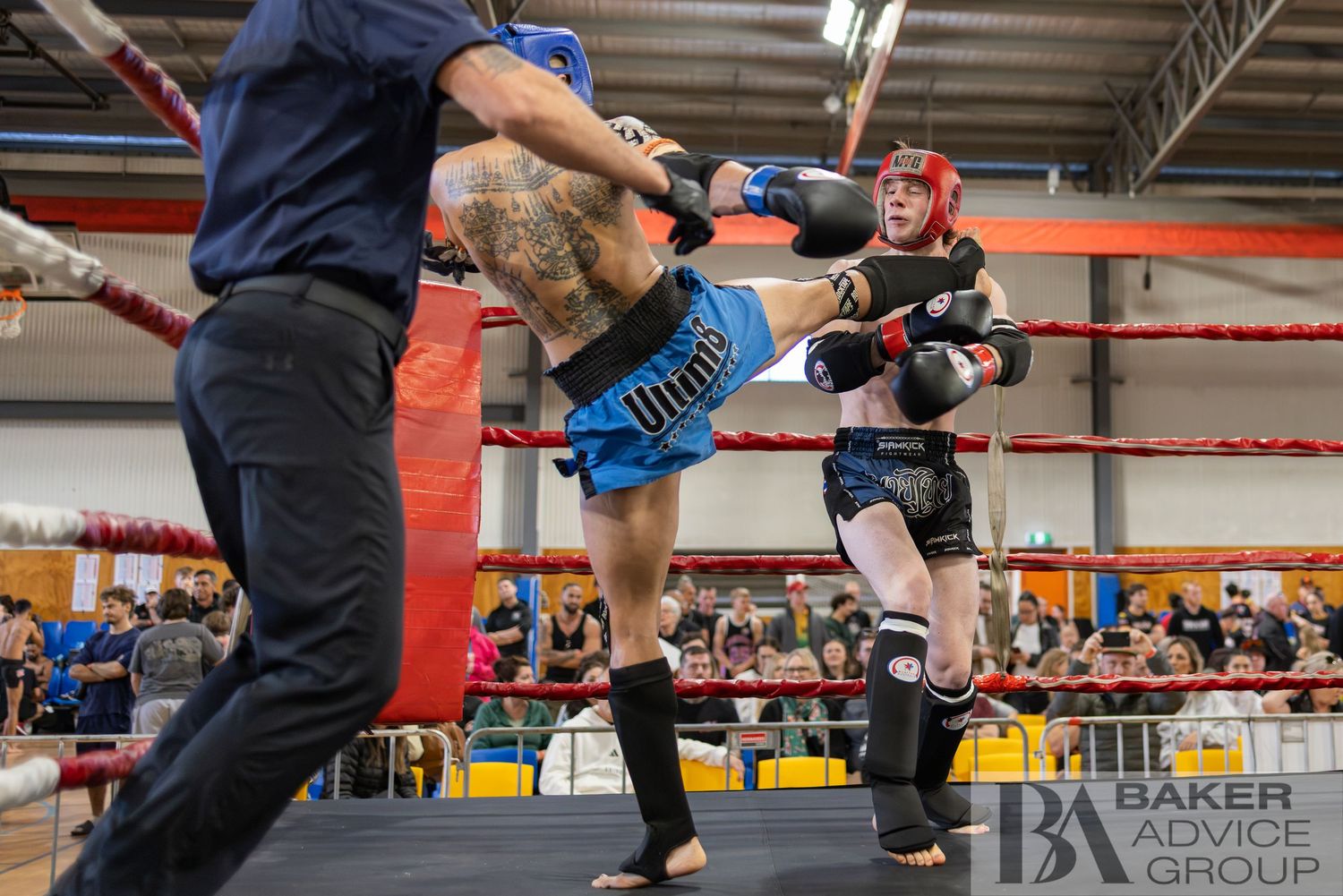 Two Muay Thai fighters compete in a ring match, with one landing a kick while a referee watches closely.