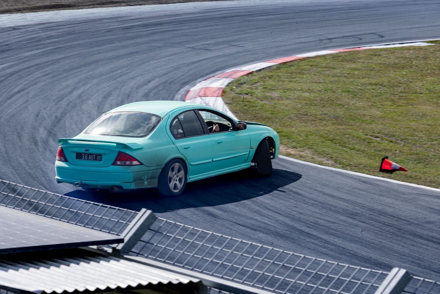A teal sedan racing around a curve on a professional motorsport track.