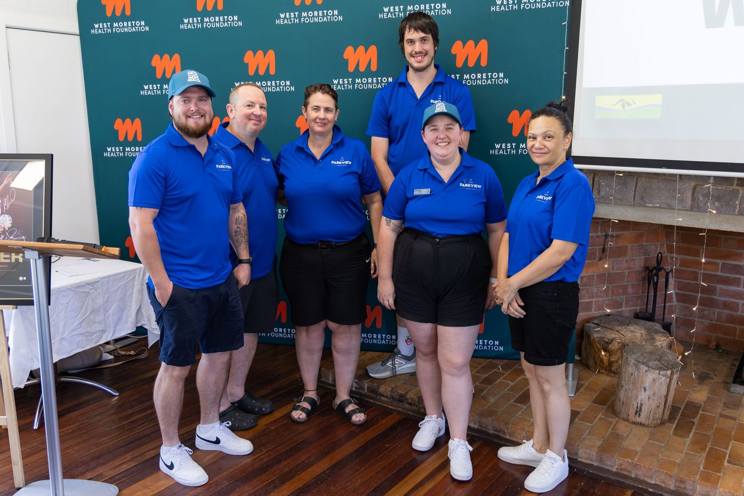 Six staff members in blue polo shirts smile together at a West Monroe Partners corporate event indoors.