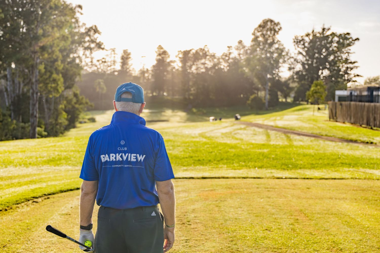Golfer in Parkview blue shirt and cap stands on sunny golf course fairway holding a club.