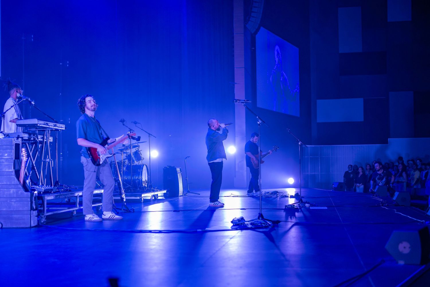 Band performing on stage under blue lights at a live concert venue with guitarist and vocalist.