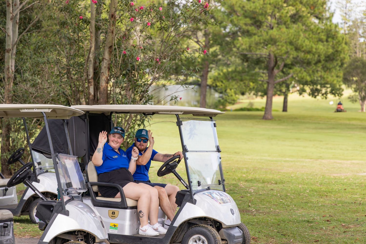 Two women smiling and posing in a white golf cart on a lush green golf course.