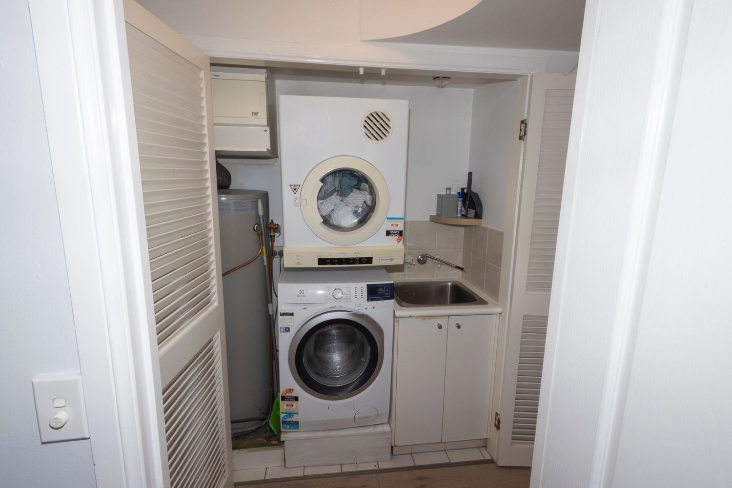 Compact laundry closet with stacked washer and dryer units above a front-load washing machine beside a small sink.